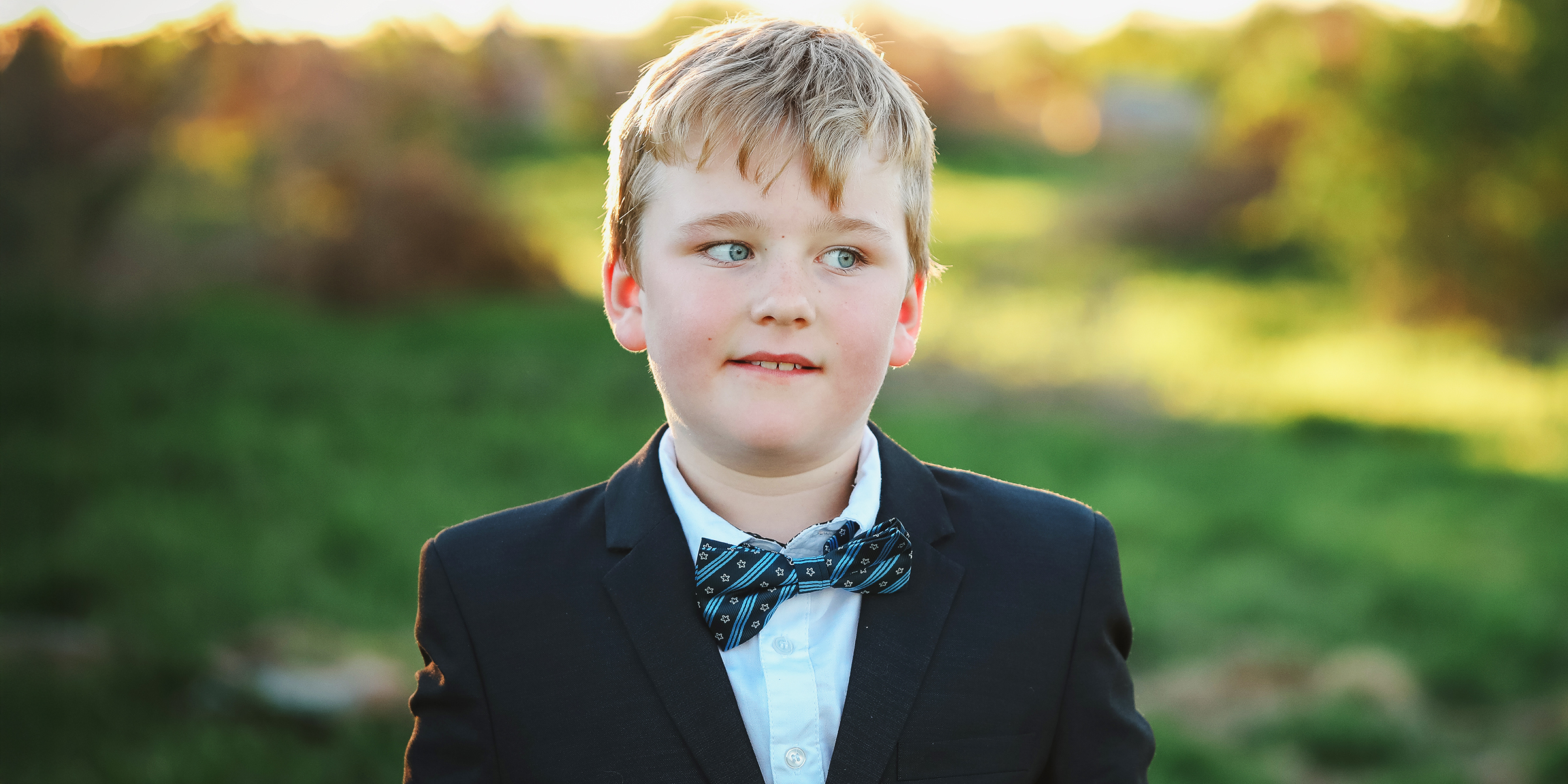 Un chico joven con traje y pajarita de pie al aire libre | Fuente: Shutterstock