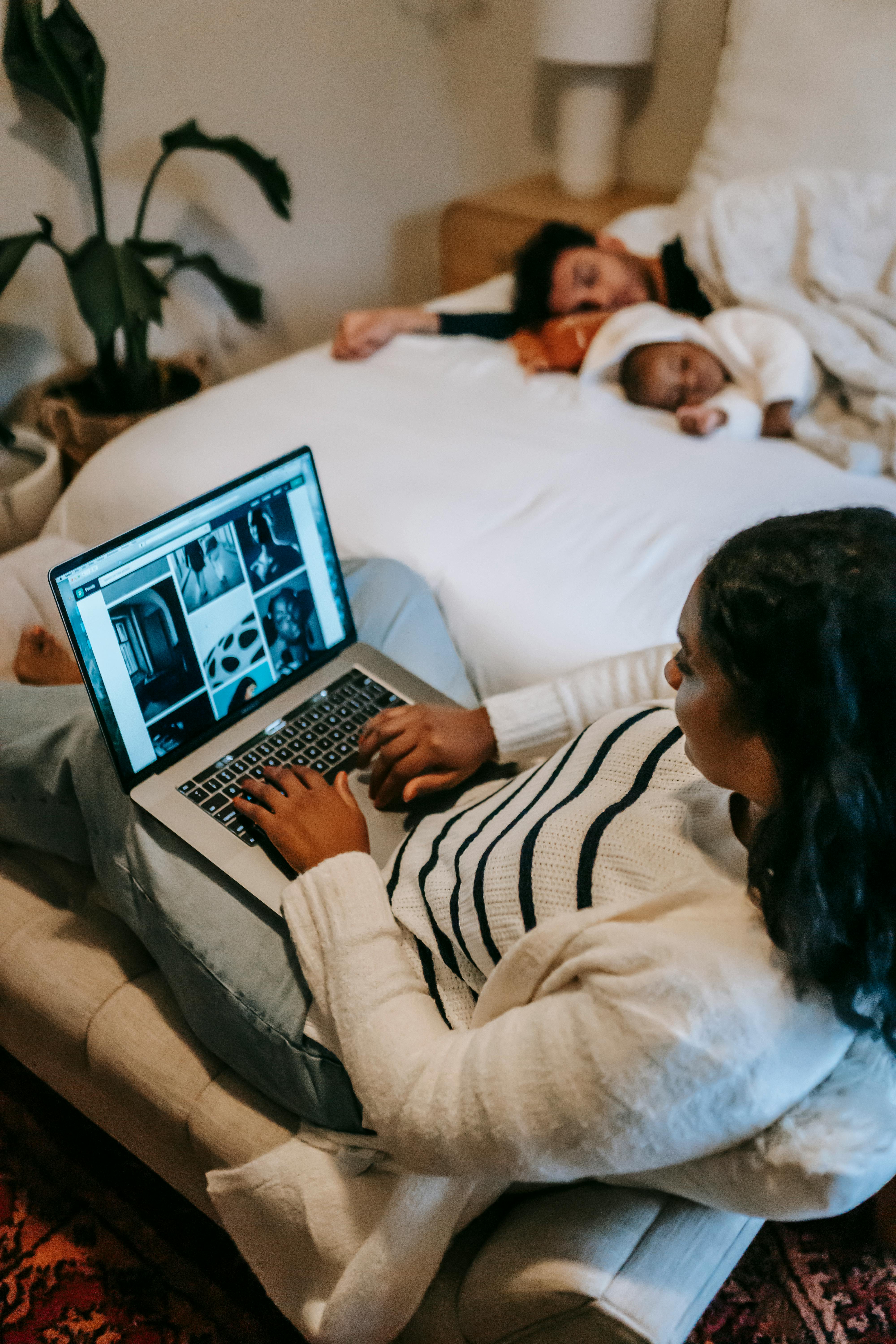 Una mujer con su portátil y su familia durmiendo en la cama | Fuente: Pexels
