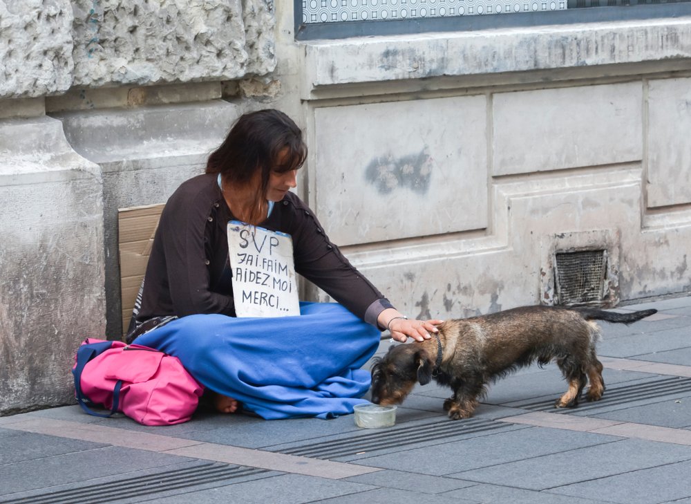 Mujer indigente compartiendo sus alimentos con un perrito de la calle. | Foto: Shutterstock.