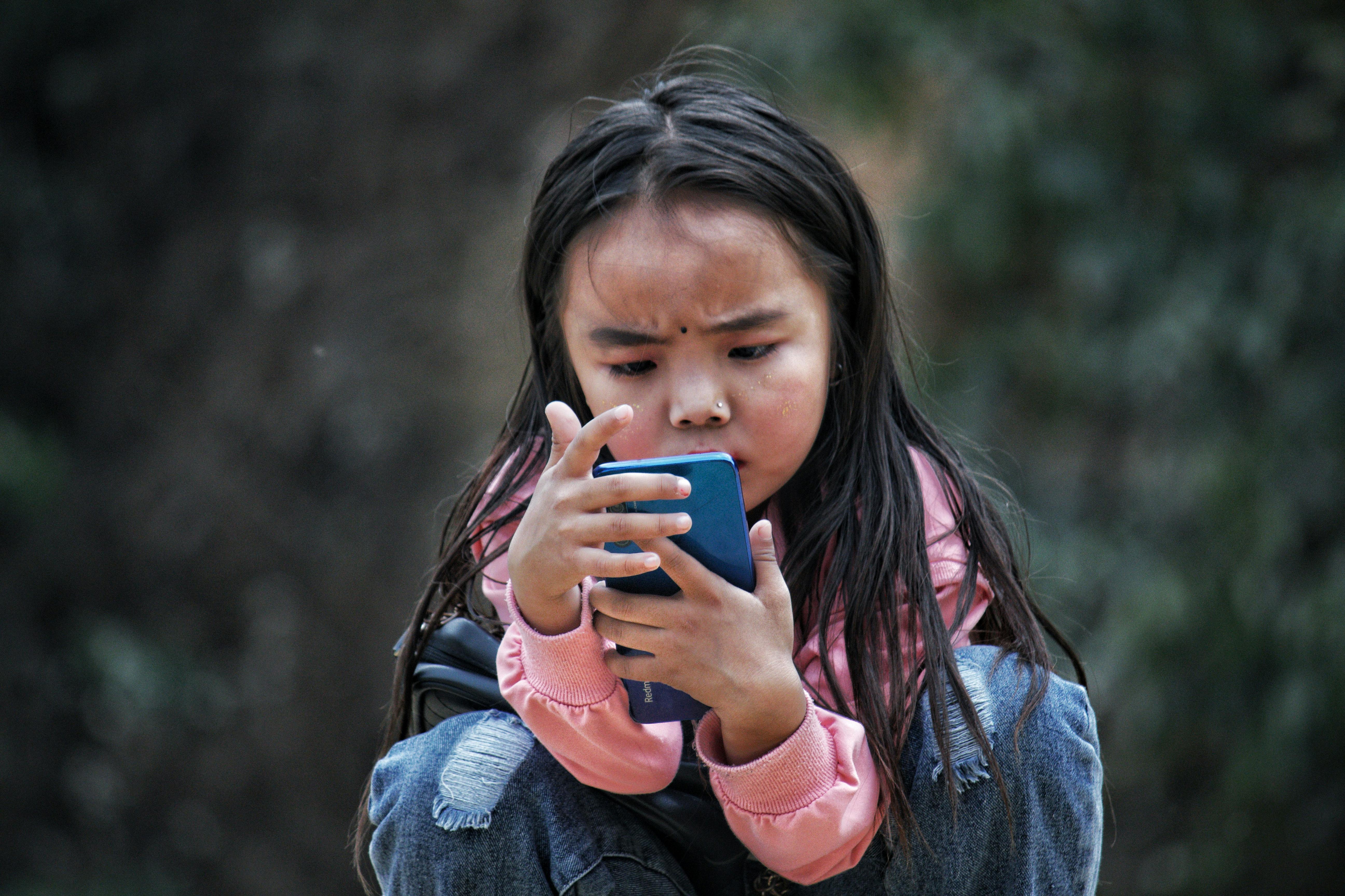 Una niña jugueteando con un móvil | Fuente: Pexels