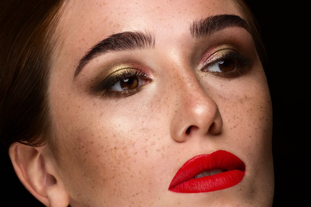 Modelo pecosa con labial rojo, sombras oscuras en los párpados y cejas gruesas. | Foto: Shutterstock