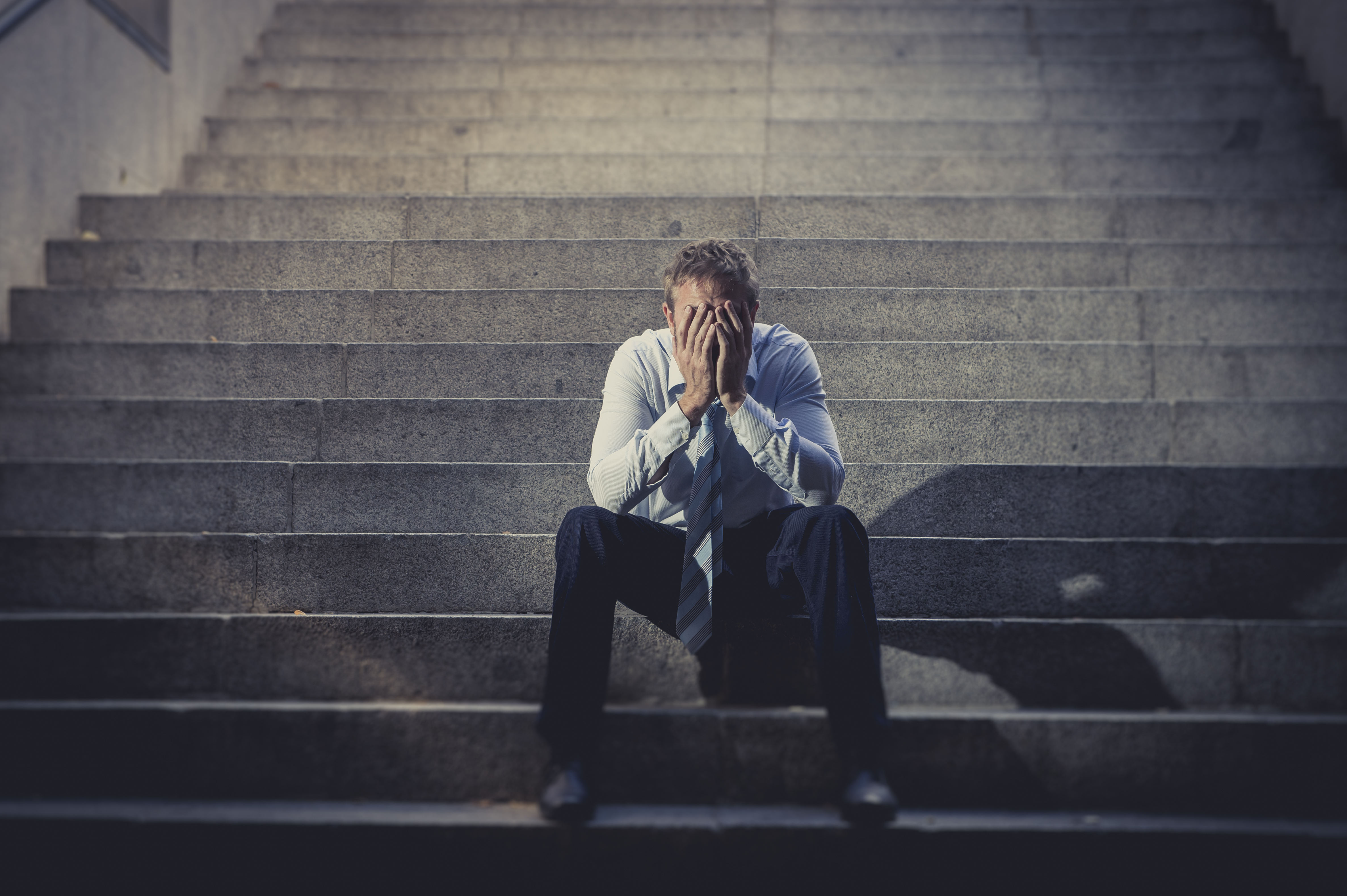 Un hombre deprimido sentado en unas escaleras de hormigón | Foto: Shutterstock