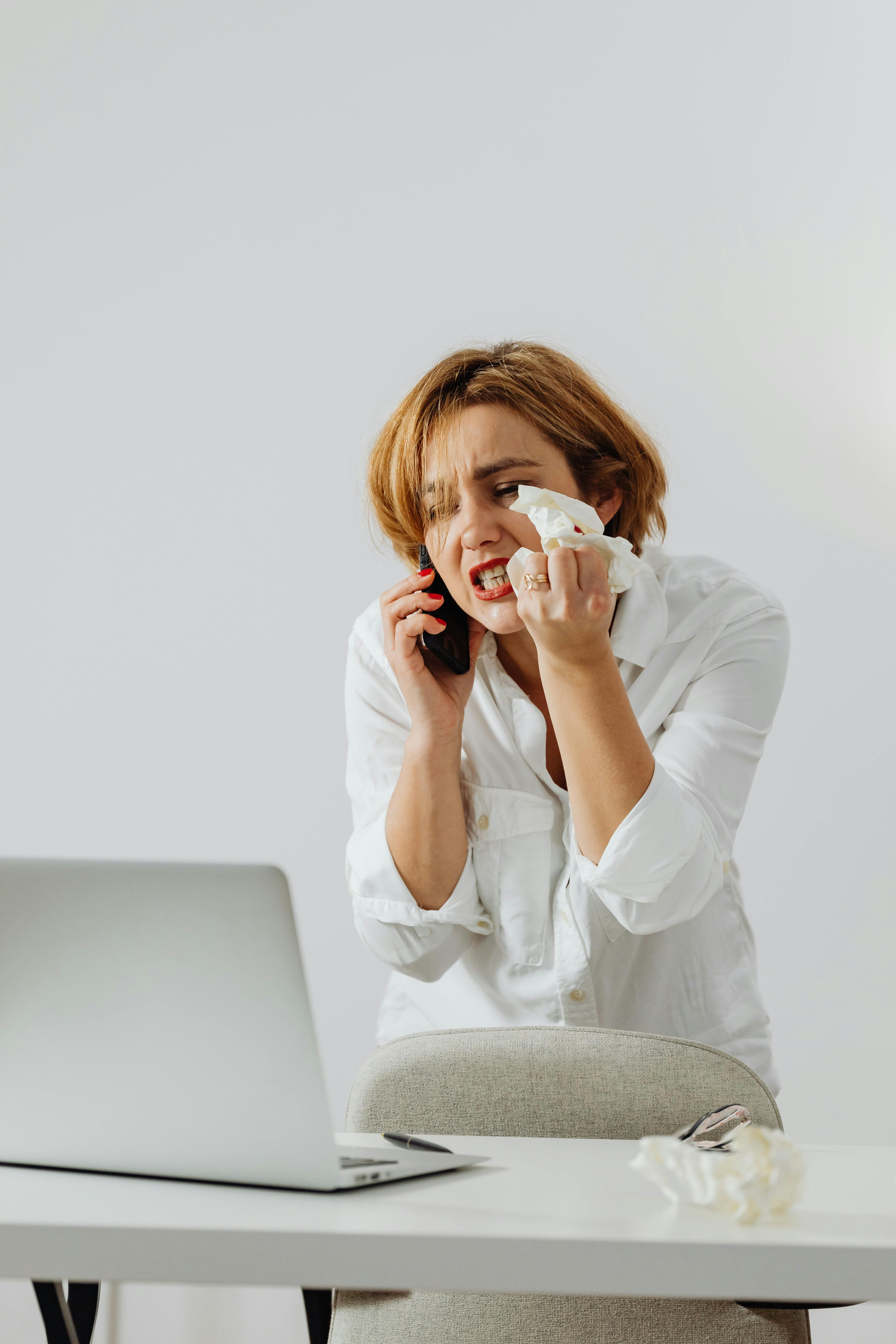 Mujer grita por teléfono delante de su portátil | Fuente: Pexels