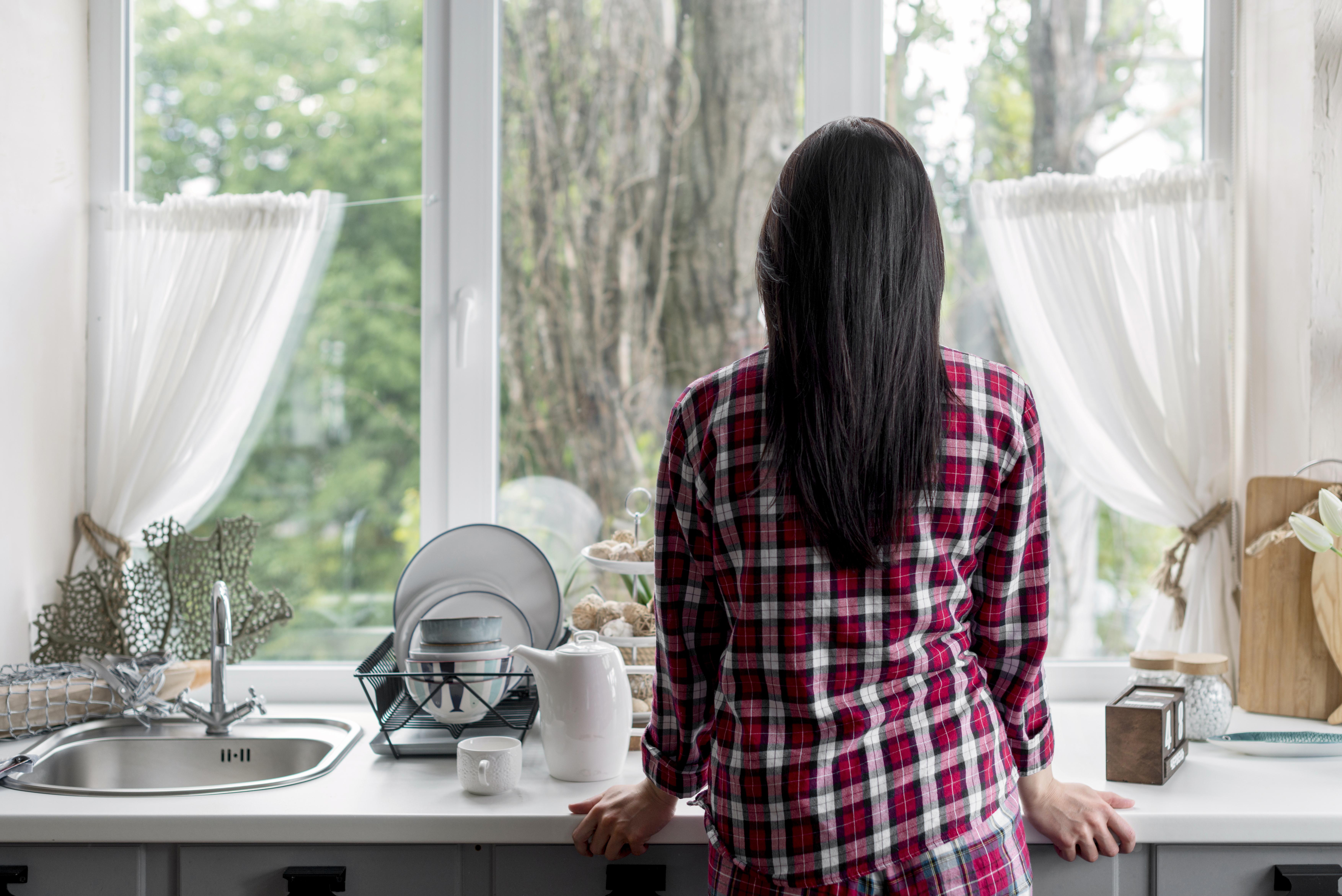 Vista trasera de una mujer mirando por la ventana de la cocina | Fuente: Freepik