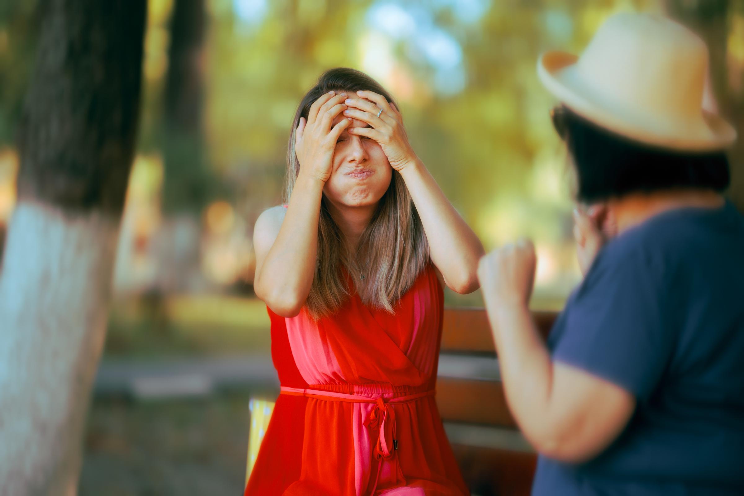 Mujer con sus manos en su rostro mientras conversa con otra mujer | Fuente: Shutterstock