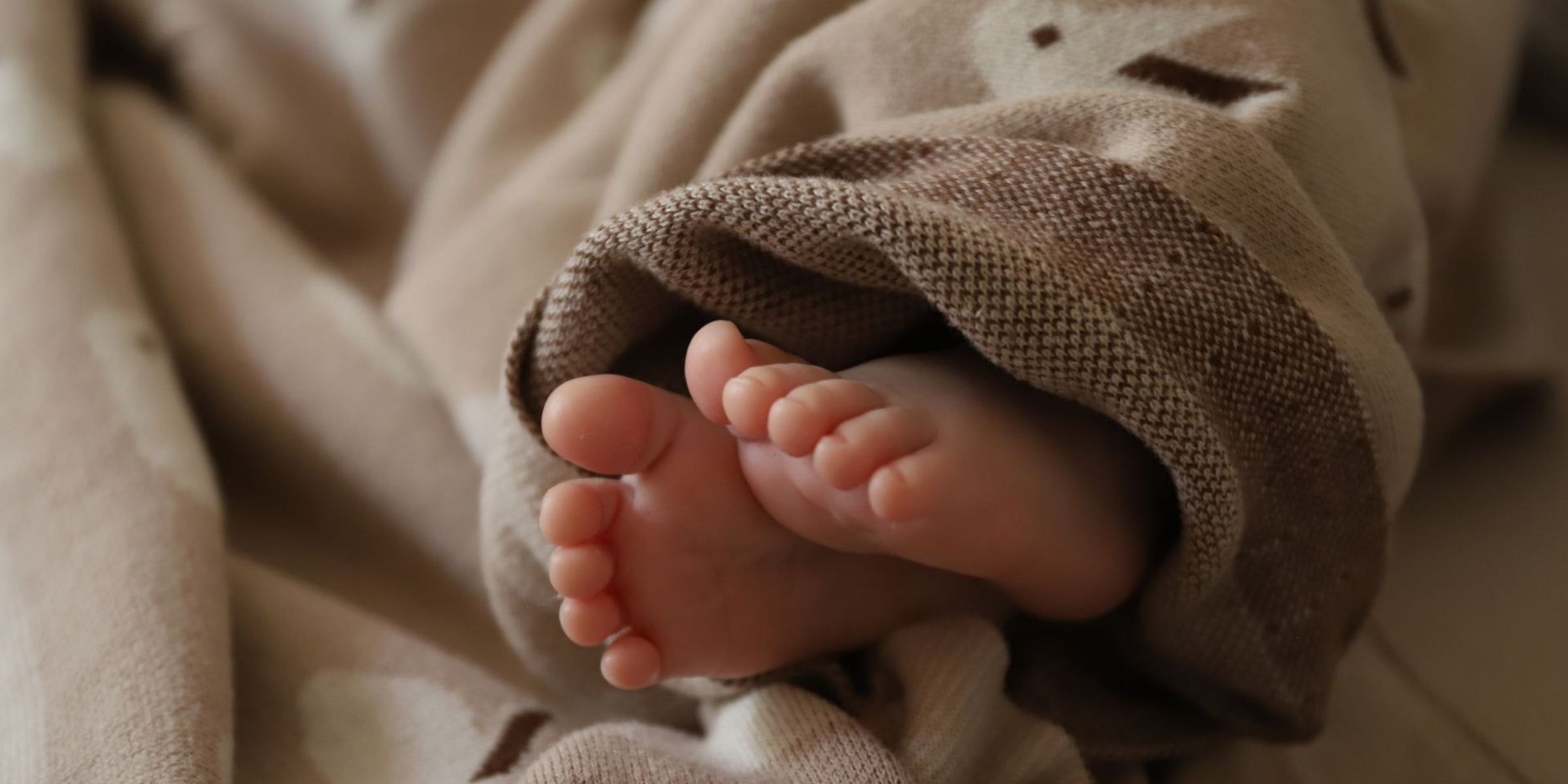 Adorabili piedini di un neonato avvolti in una morbida e calda copertina | Fonte: Pexels