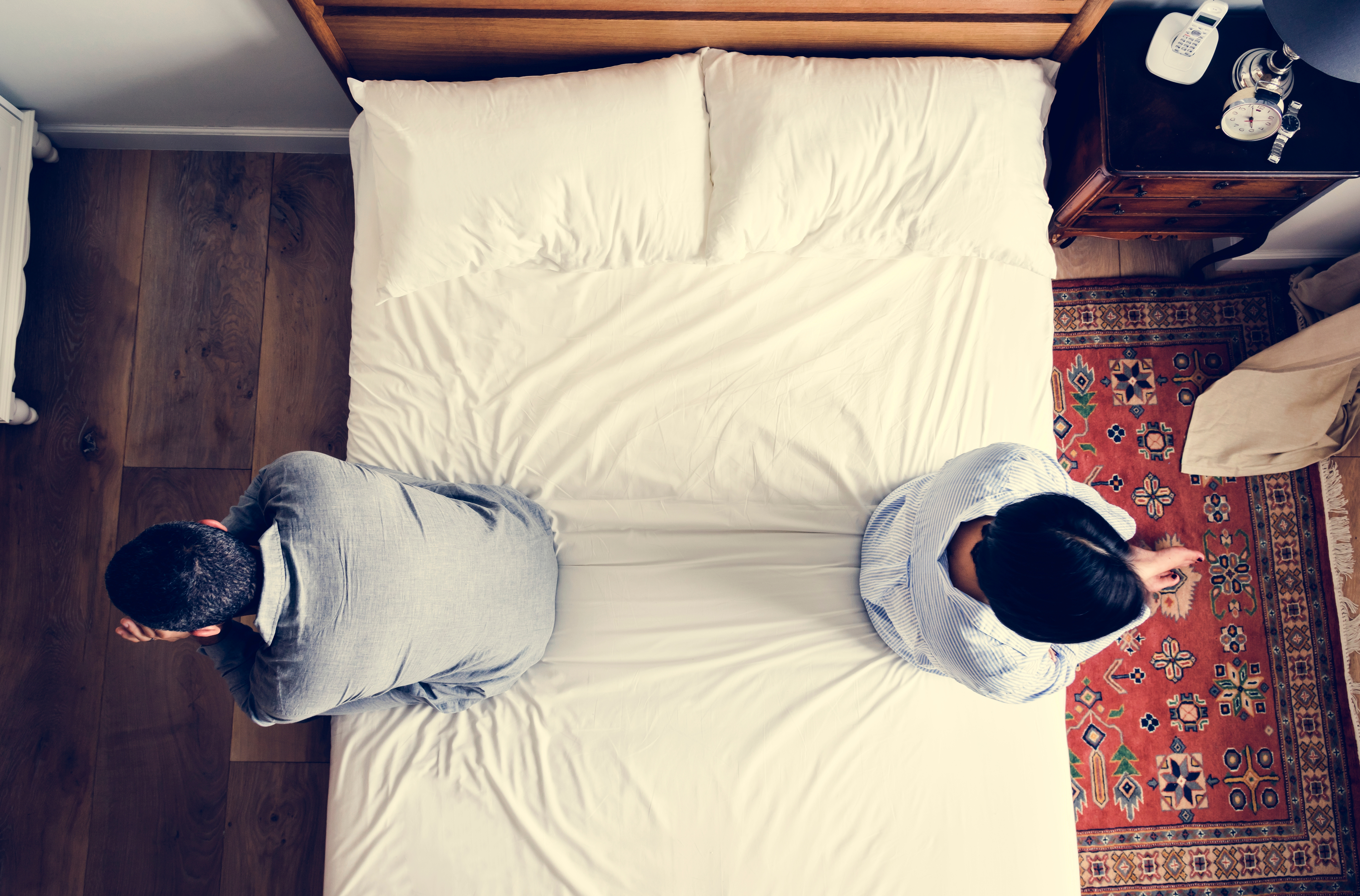 Una pareja sentada en extremos opuestos de la cama tras una discusión | Foto: Shutterstock