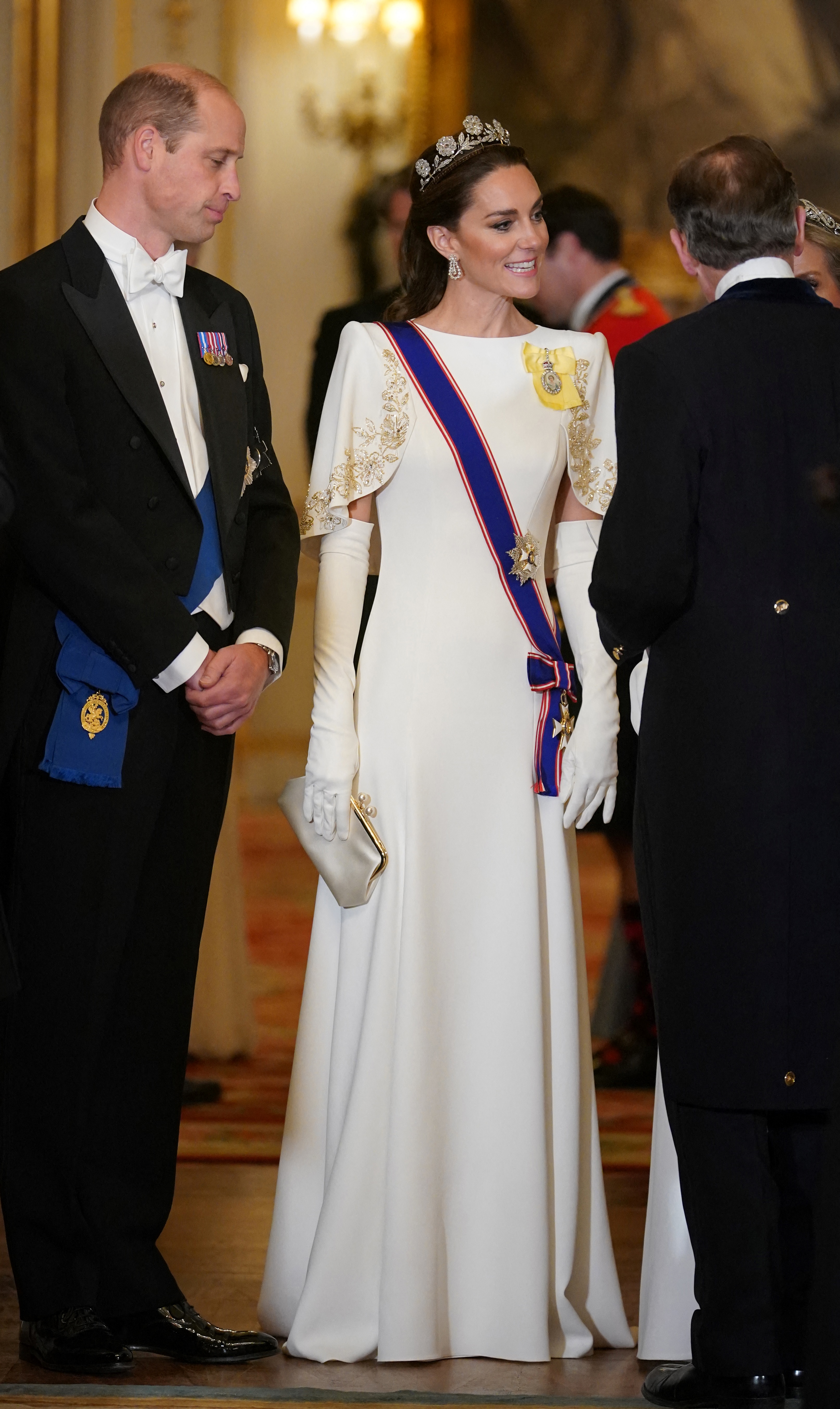 El príncipe William y Catherine, princesa de Gales, llegan al banquete de Estado en honor al presidente surcoreano Yoon Suk Yeol y la primera dama Kim Keon Hee, en el Palacio de Buckingham el 21 de noviembre de 2023. Catherine deslumbra con un vestido blanco a medida de Jenny Packham, con mangas cortas bordadas en dorado, guantes largos blancos, la histórica tiara Strathmore Rose, pendientes de diamantes de la reina Elizabeth II e insignias reales. William la acompaña con frac negro clásico y corbata blanca. | Fuente: Getty Images