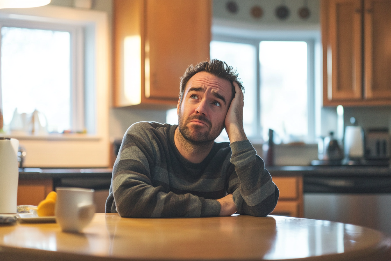 Un hombre sentado en una cocina con cara de confusión | Fuente: Midjourney