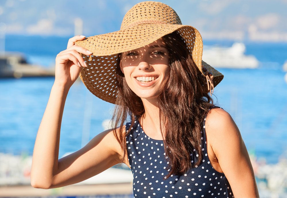 Mujer en la playa cubriendo su cabello con un sombrero. | Foto: Shutterstock