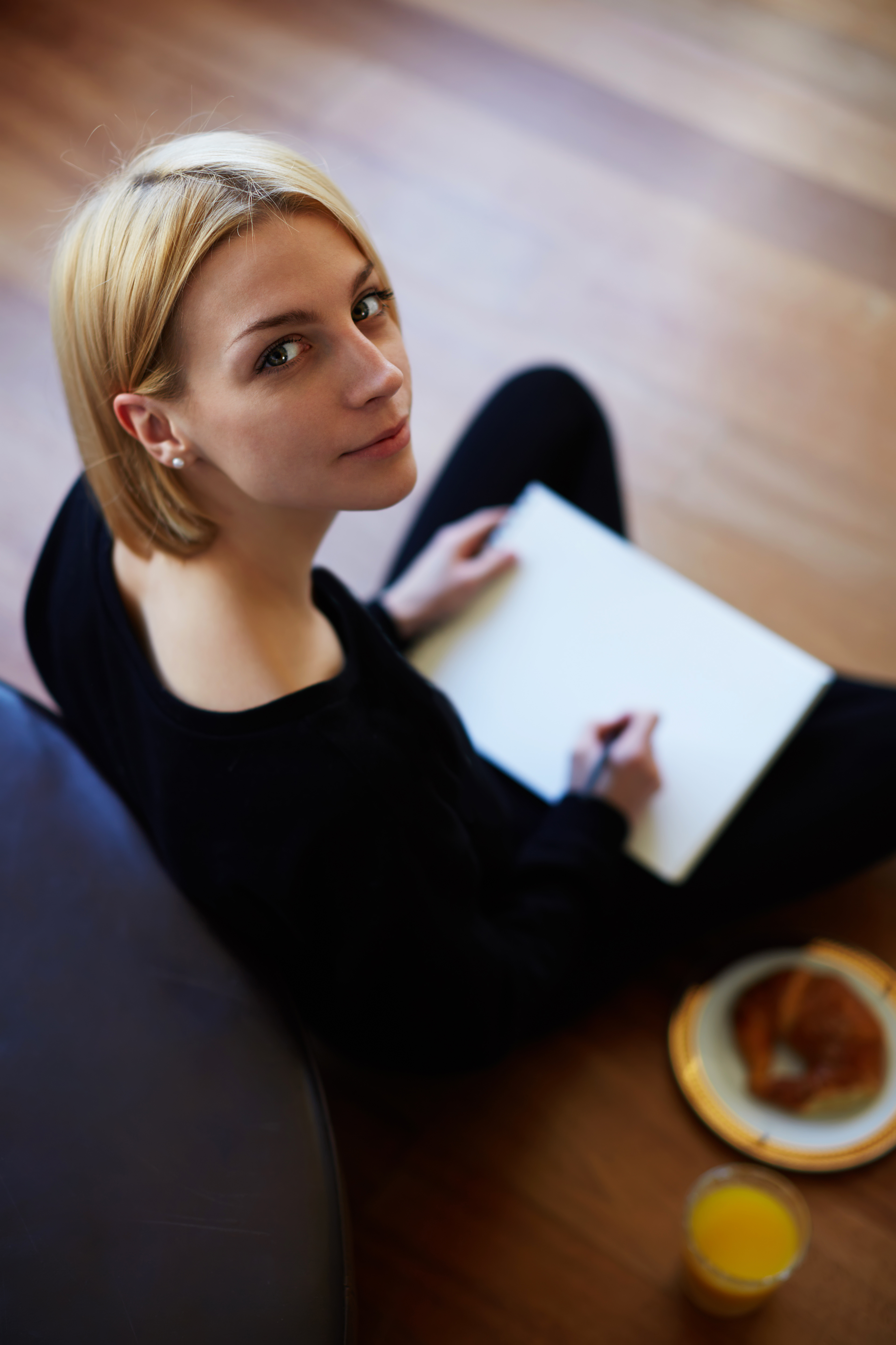 Vista superior de una joven rubia dibujando en un papel sentada en el suelo del salón | Fuente: Shutterstock.com