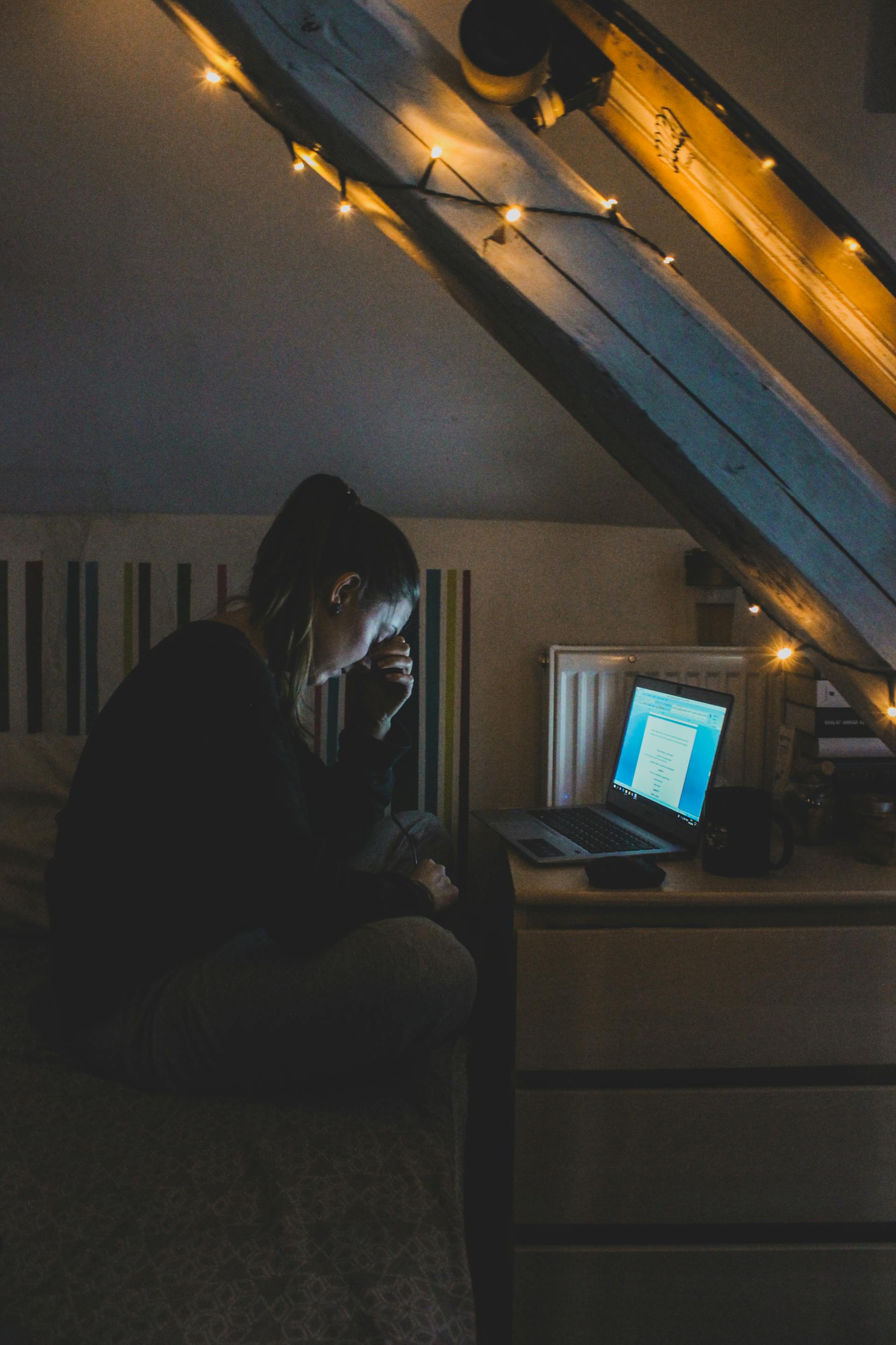 Un plano lejano de una mujer que parece angustiada mientras utiliza su portátil por la noche | Fuente: Pexels