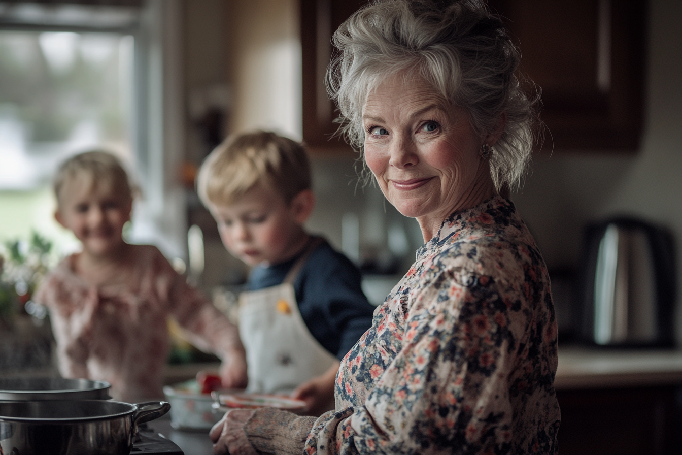 Mujer de unos 60 años sonriendo y cocinando en una cocina con dos niños al fondo | Fuente: Midjourney