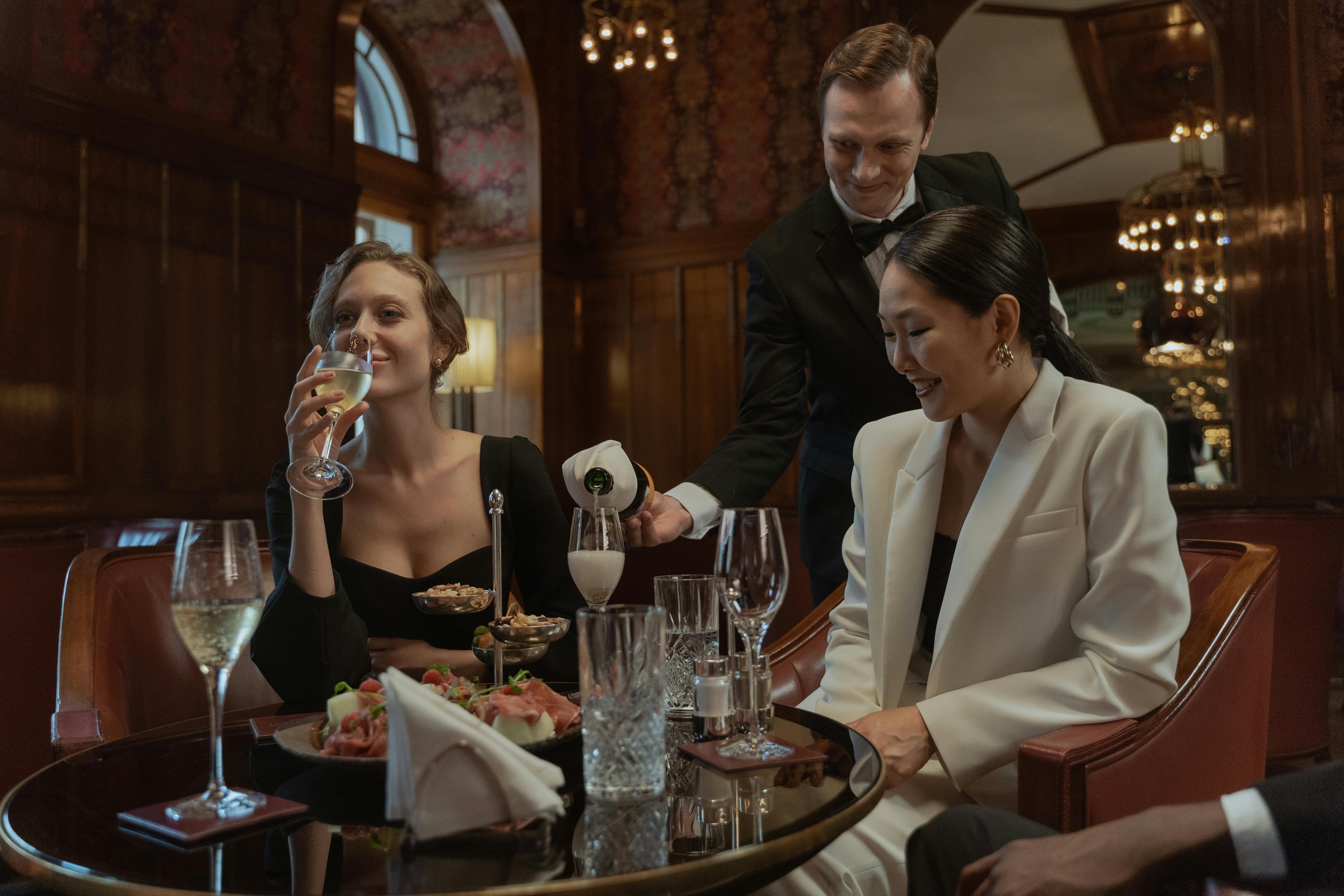 Mujeres disfrutando de unas copas mientras un camarero les sirve | Foto: Pexels