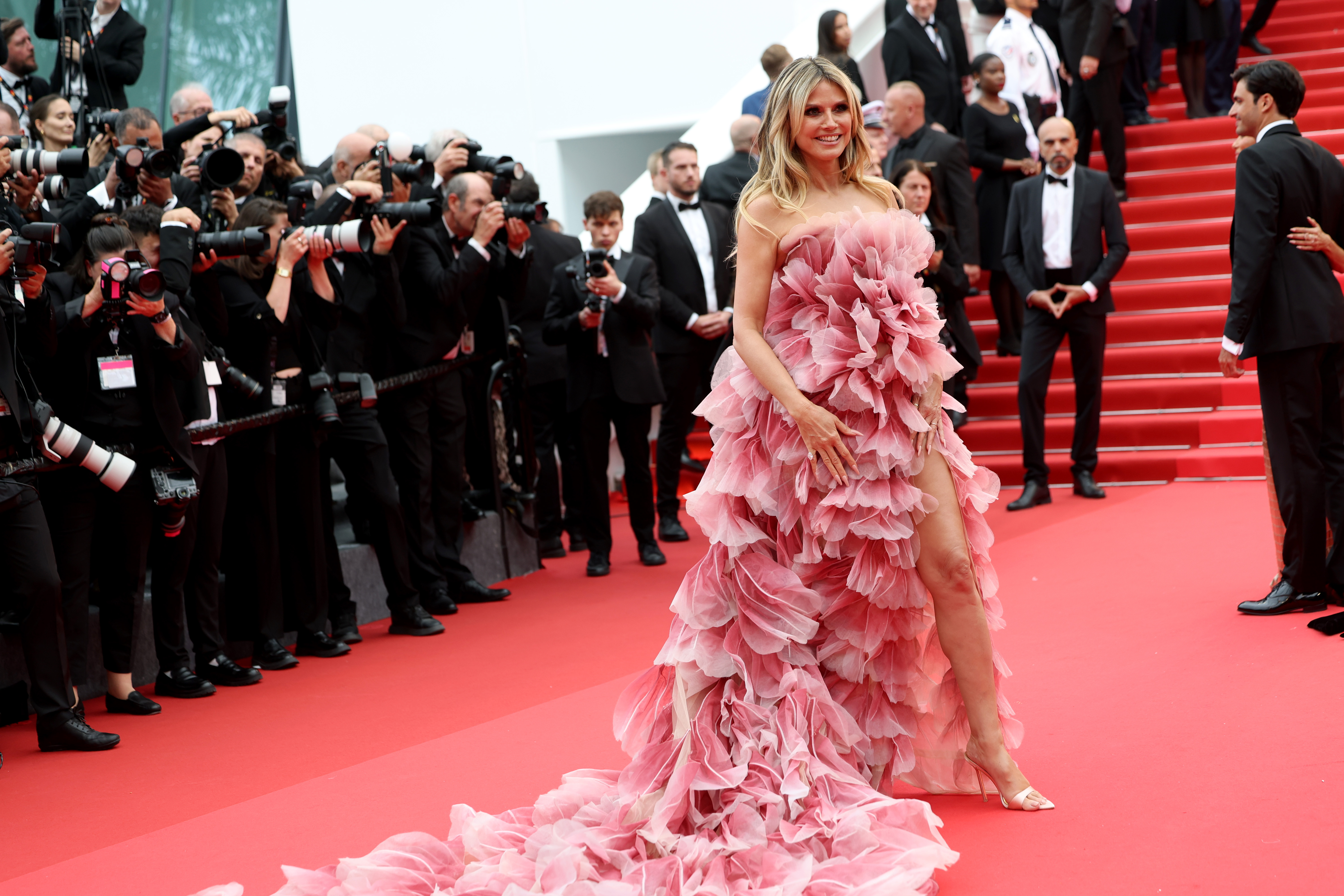 Klum sonríe, saboreando claramente el momento y la atención que conlleva. Una pierna asoma por la abertura hasta el muslo de su vestido, dejando ver un brillante tacón de aguja plateado que añade dramatismo a su look.