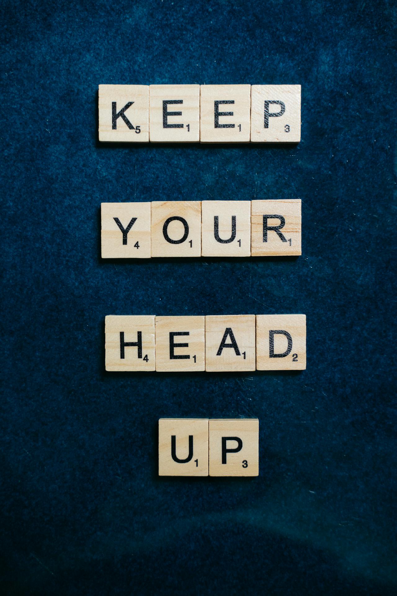 Fichas de Scrabble con la frase "MANTÉN LA CABEZA EN ALTO" | Fuente: Pexels