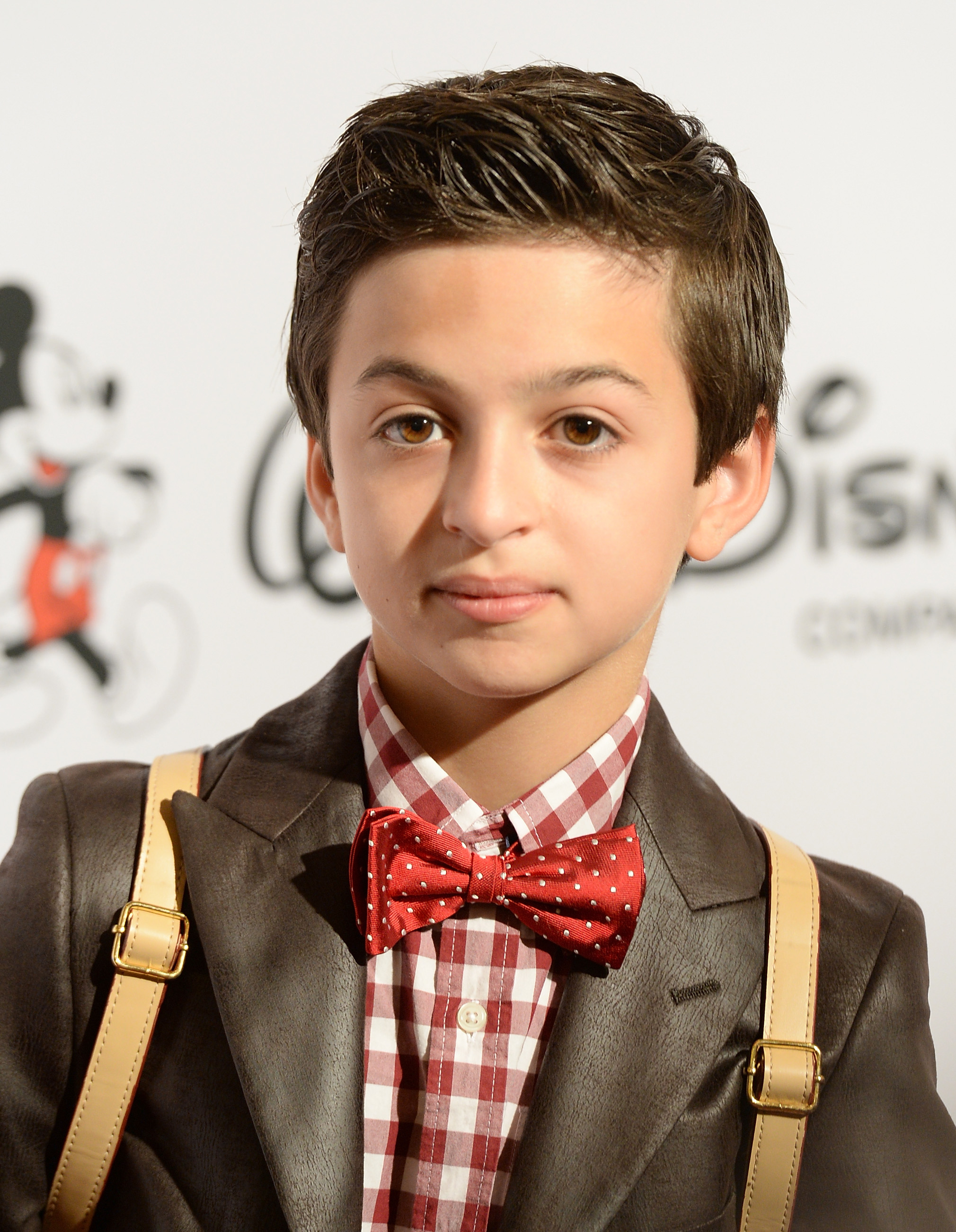 Llega a la 9ª edición de los Premios Respect de GLSEN, en el Hotel Beverly Hills de Beverly Hills, California, con una chaqueta marrón oscuro, una camisa a cuadros rojos y blancos, una pajarita roja a juego y tirantes de color beige. | Fuente: Getty Images