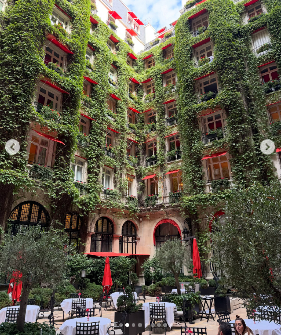 La vista del patio interno de un lujoso hotel revela una impresionante fachada tapizada de enredaderas verdes y balcones con toldos rojos, rodeada de mesas preparadas al aire libre entre frondosos arbustos. | Fuente: Instagram/juliana.awada