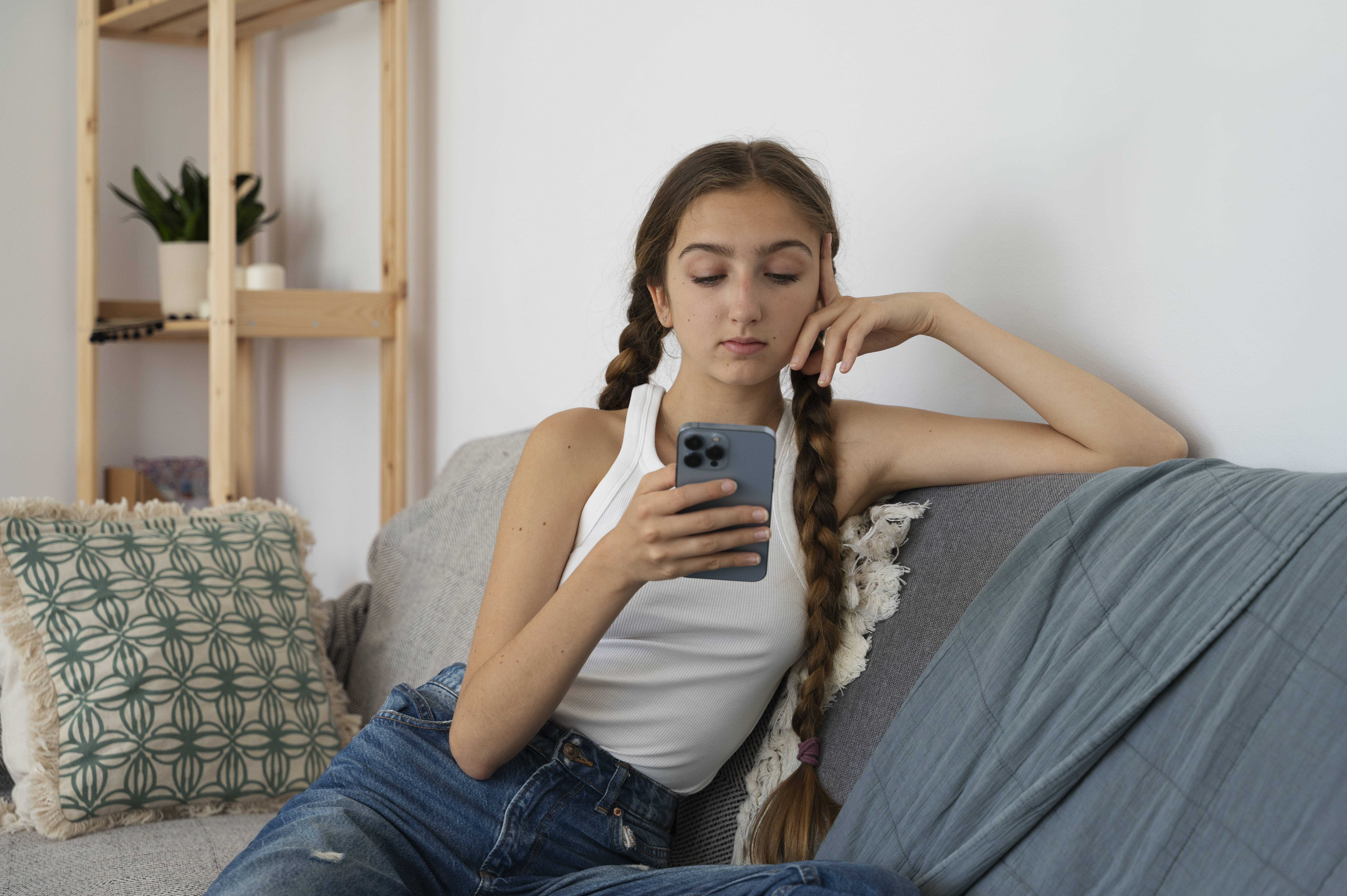 Chica joven sentada en un sofá y mirando su móvil | Fuente: Freepik