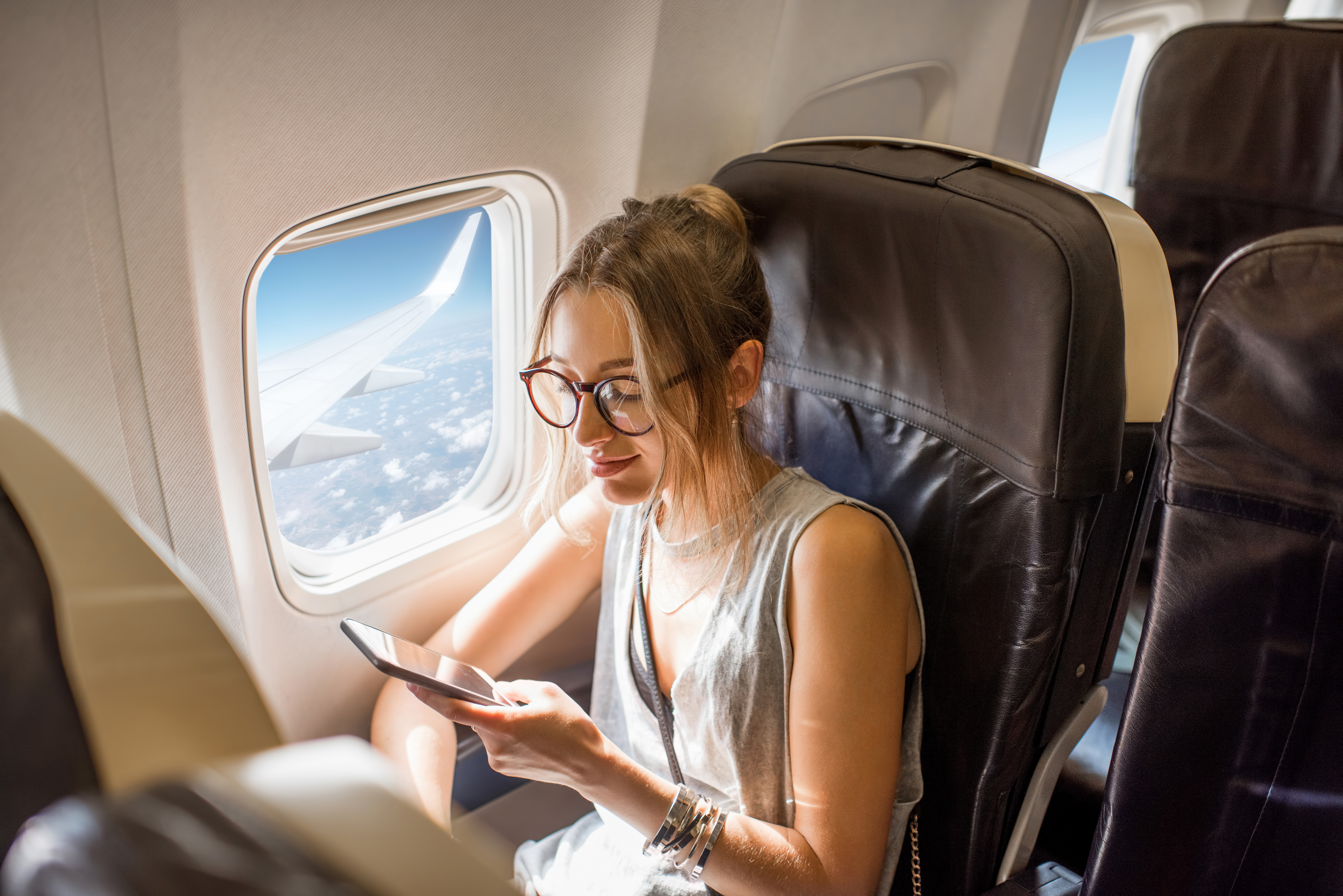 Mujer viendo su teléfono en un avión | Fuente: Shutterstock