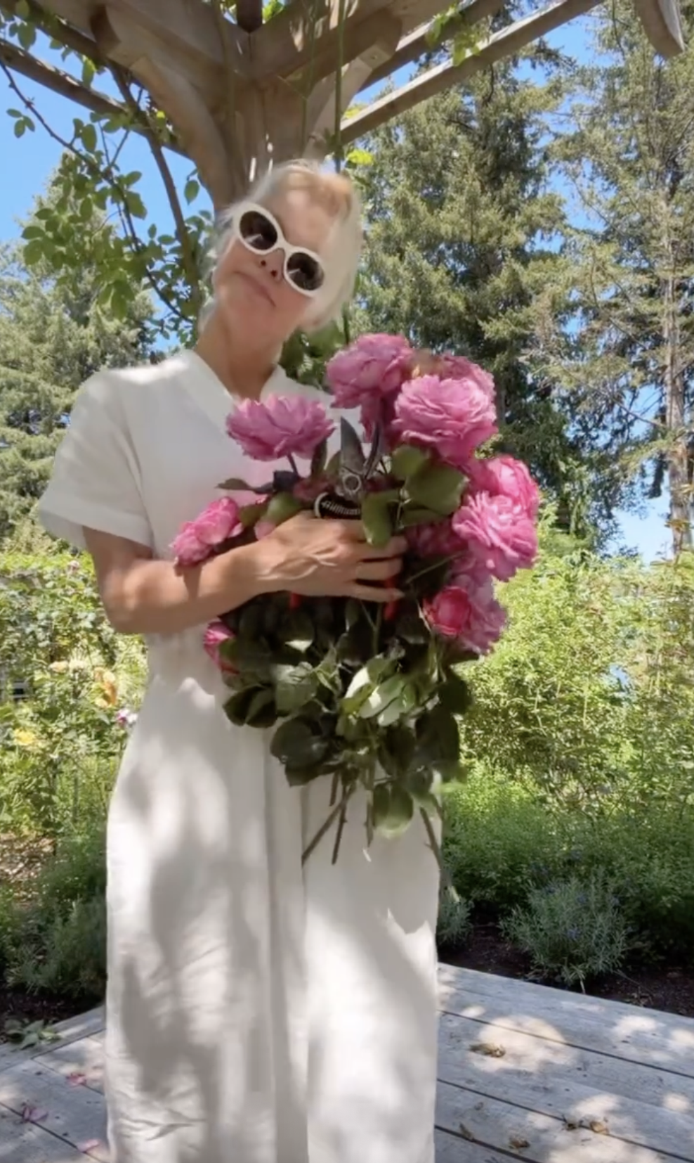 Pamela Anderson posa de forma divertida bajo una pérgola en Arcady, con unas tijeras de podar y un enorme ramo de rosas rosas recién cortadas contra su vestido blanco de lino. Con unas llamativas gafas de sol blancas y ovaladas, encarna con naturalidad la alegría de cultivar sus propias flores, mostrando con orgullo las flores recogidas en su floreciente santuario de 15 000 pies cuadrados. | Fuente: Instagram/pamelaanderson