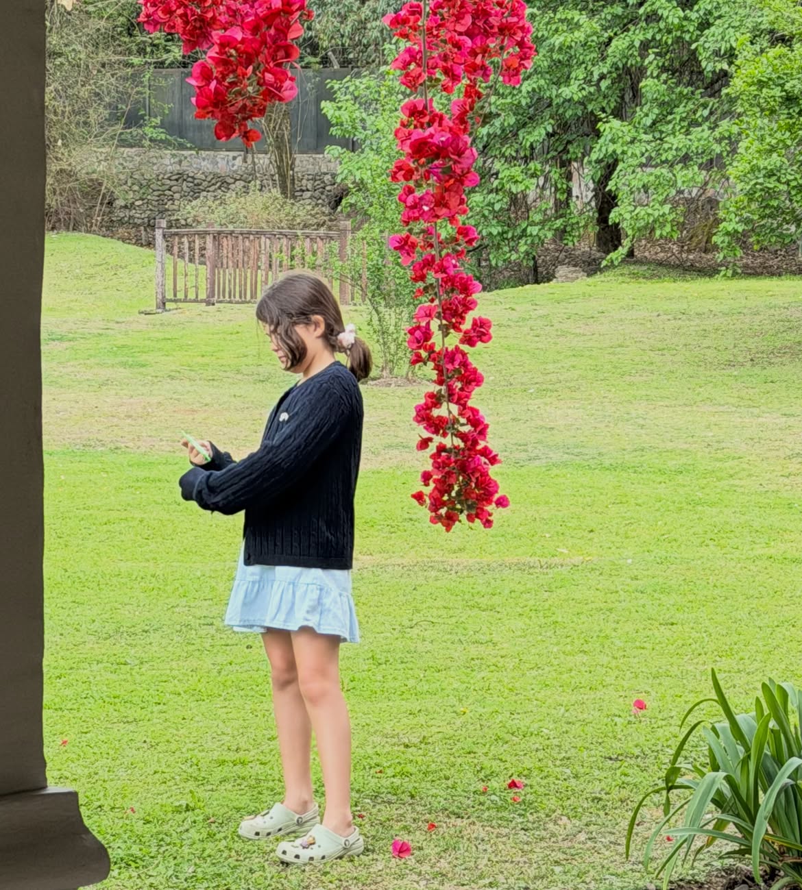Belita, la hija mayor de Isabel Macedo, posando de pie en un paisaje con pasto verde y árboles florales | Fuente: Instagram/isabelmacedophoto