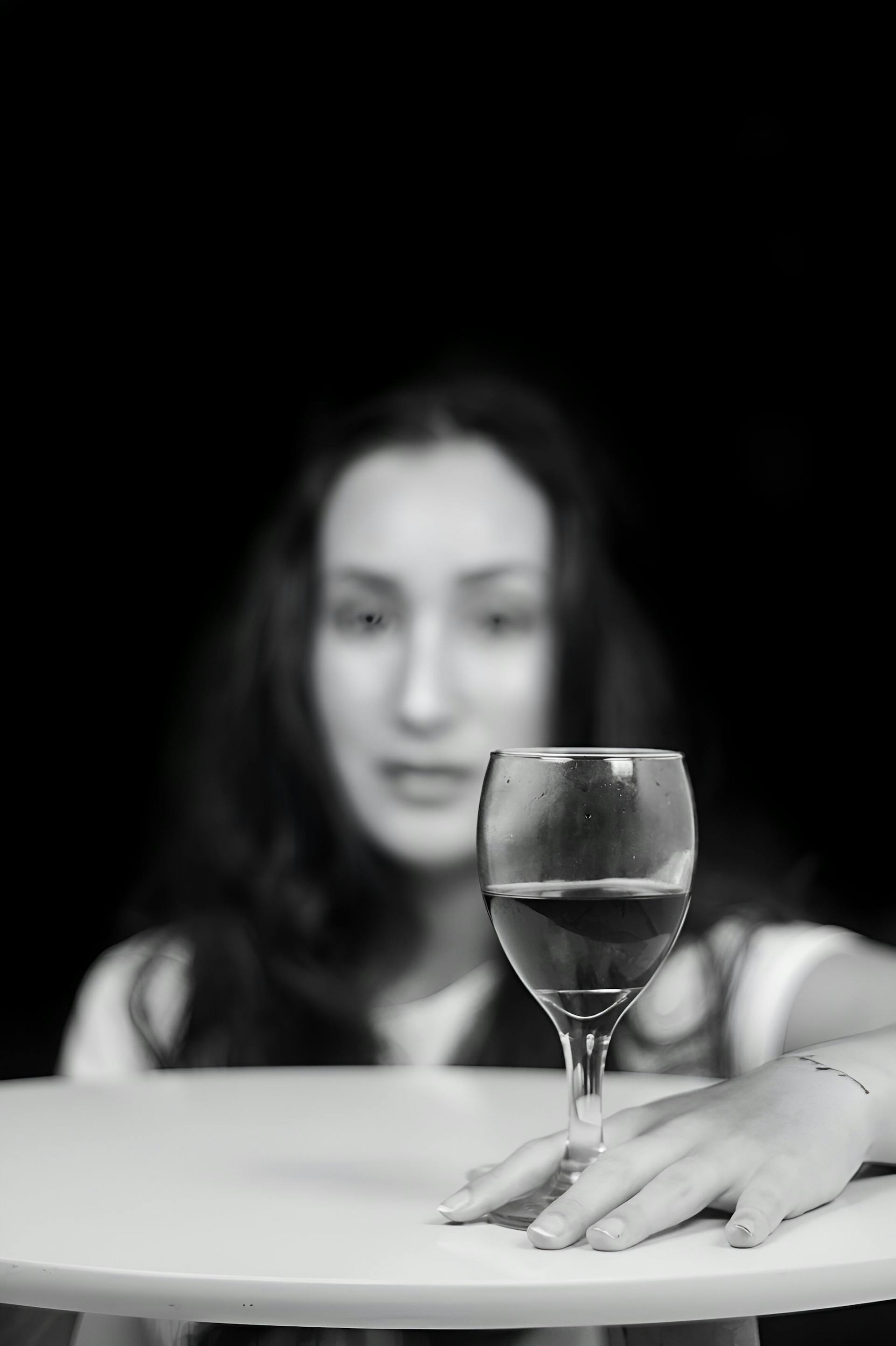 Escala de grises de una mujer sentada a la mesa con una copa de vino | Fuente: Pexels