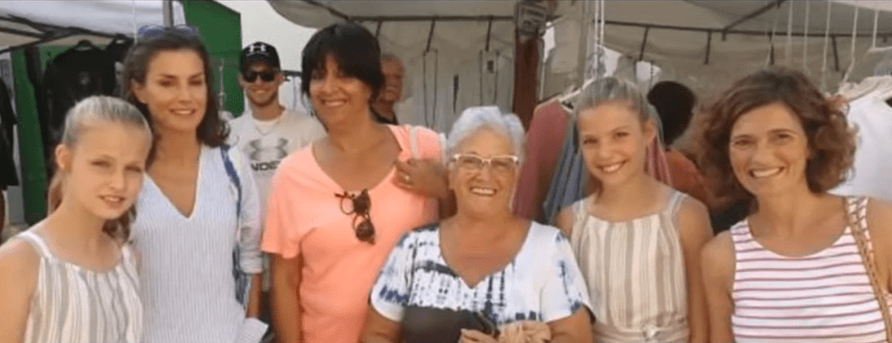 La reina Letizia de España y sus hijas, la princesa Leonor y la infanta Sofía, acompañadas pr lugareños en las calles de Pollença, en Mallorca. | Imagen: YouTube/EL ATICO BB