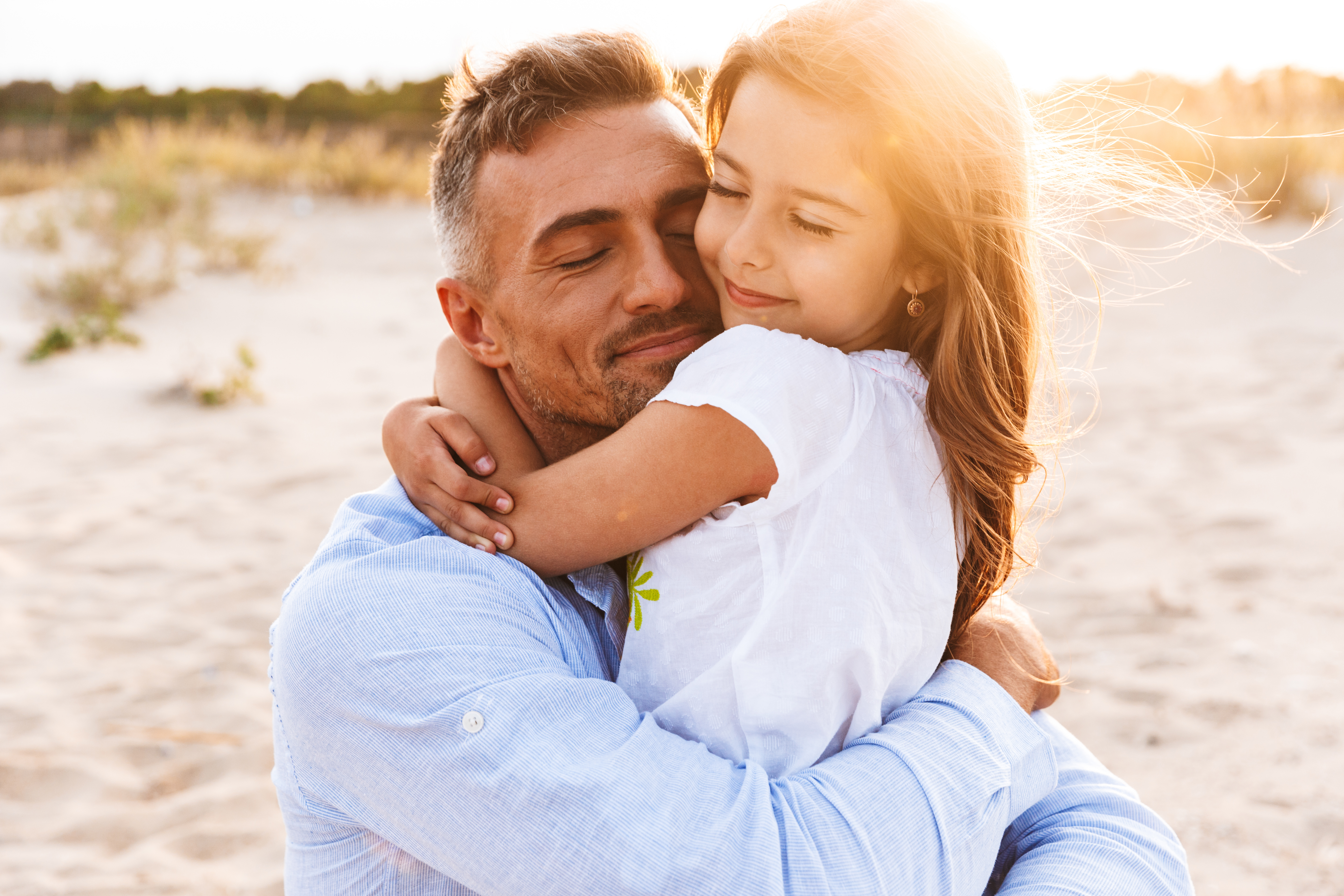 Padre feliz abrazando a su hija pequeña en la playa | Foto: Shutterstock