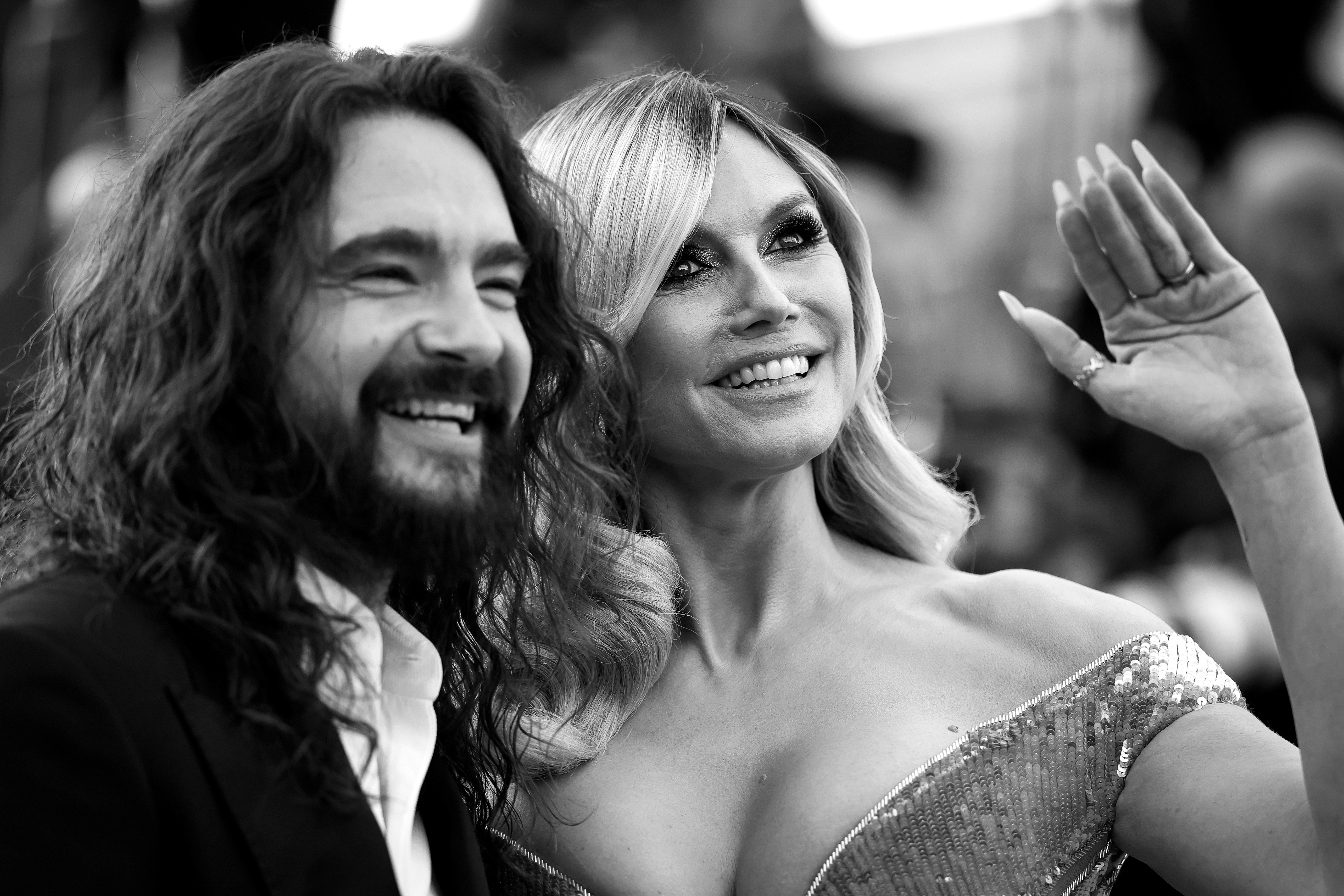 Los rostros de Kaulitz y Klum son claramente visibles cuando miran hacia la cámara. Él está radiante de orgullo y su amplia sonrisa refleja la alegría de apoyar a su esposa. A su lado, Klum levanta la mano saludando con elegancia.
