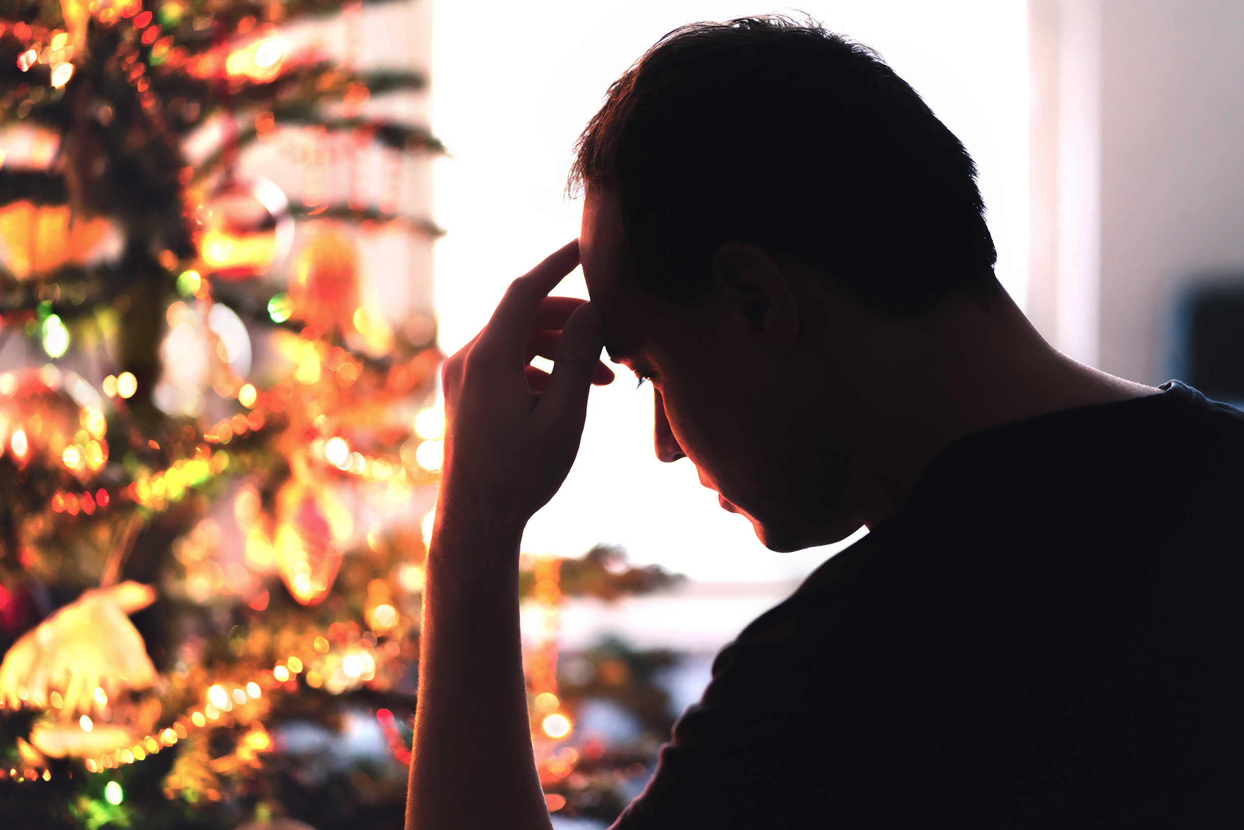 Hombre disgustado sentado delante de un árbol de Navidad | Foto: Getty Images