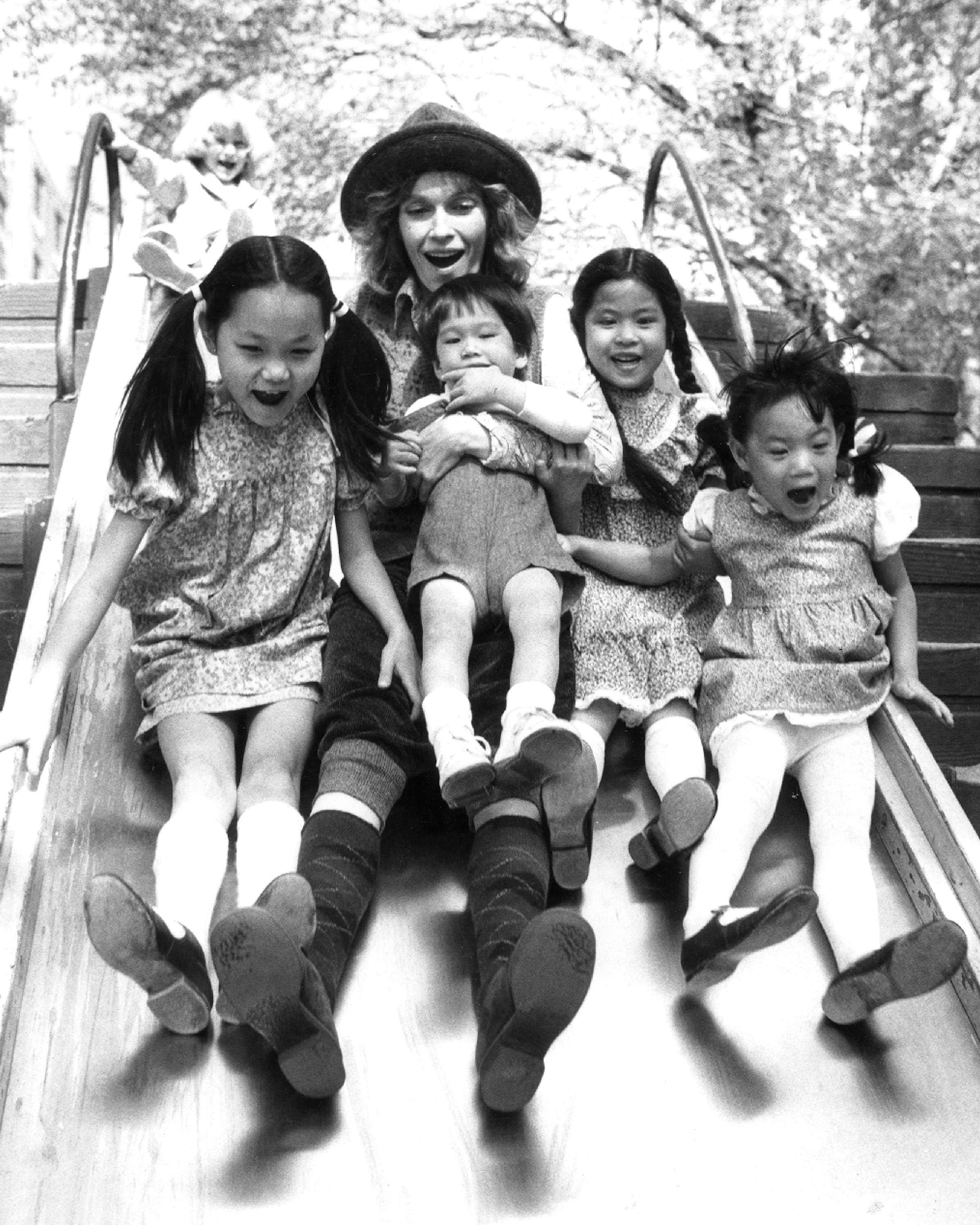 Soon Yi Previn, Mia Farrow sujetando a Misha, Lark Song y Summer, disfrutan montadas en un tobogán en Central Park, el 5 de mayo de 1980. | Fuente: Getty Images