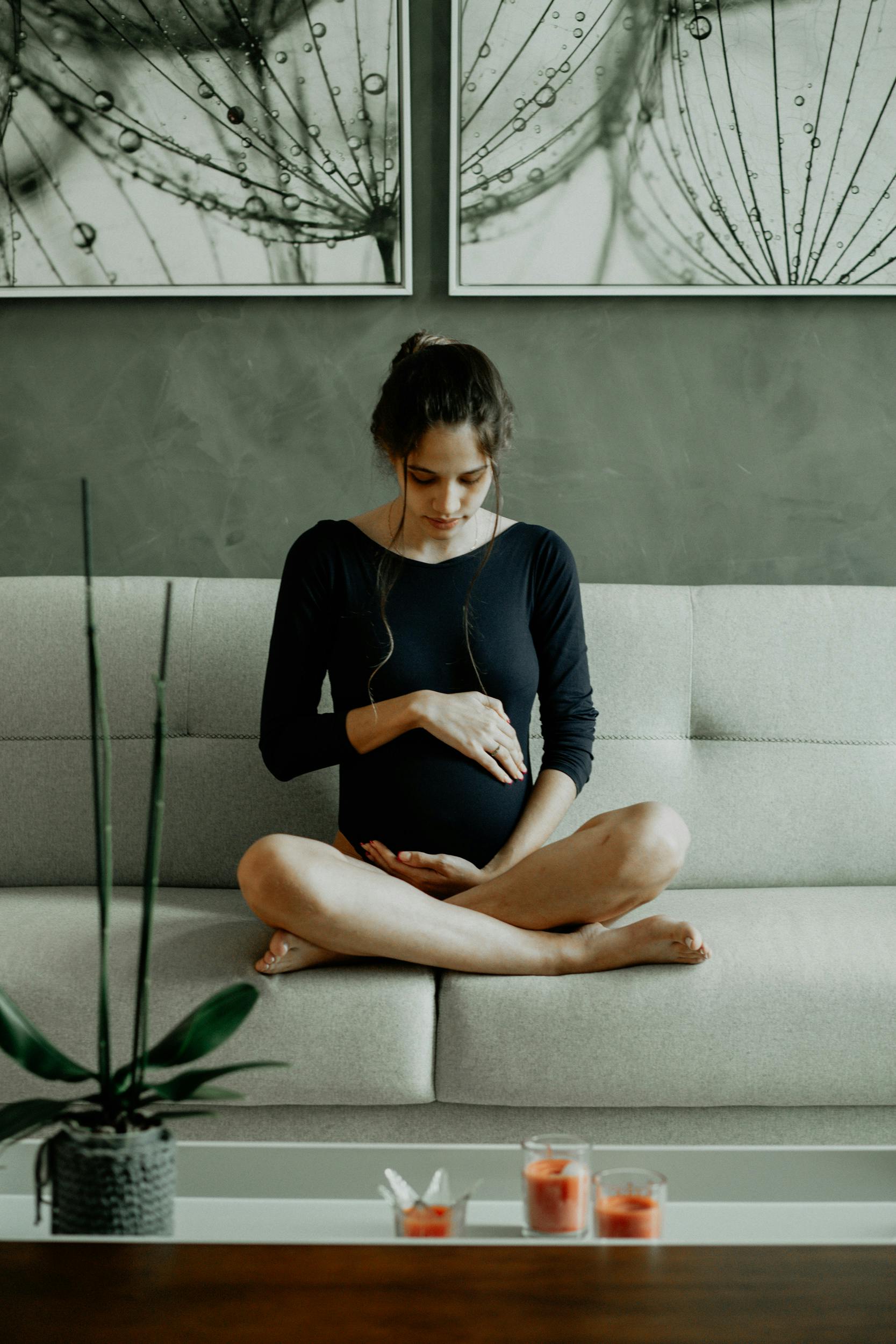 Una mujer embarazada sentada en el sofá mientras se toca la barriga | Foto: Pexels