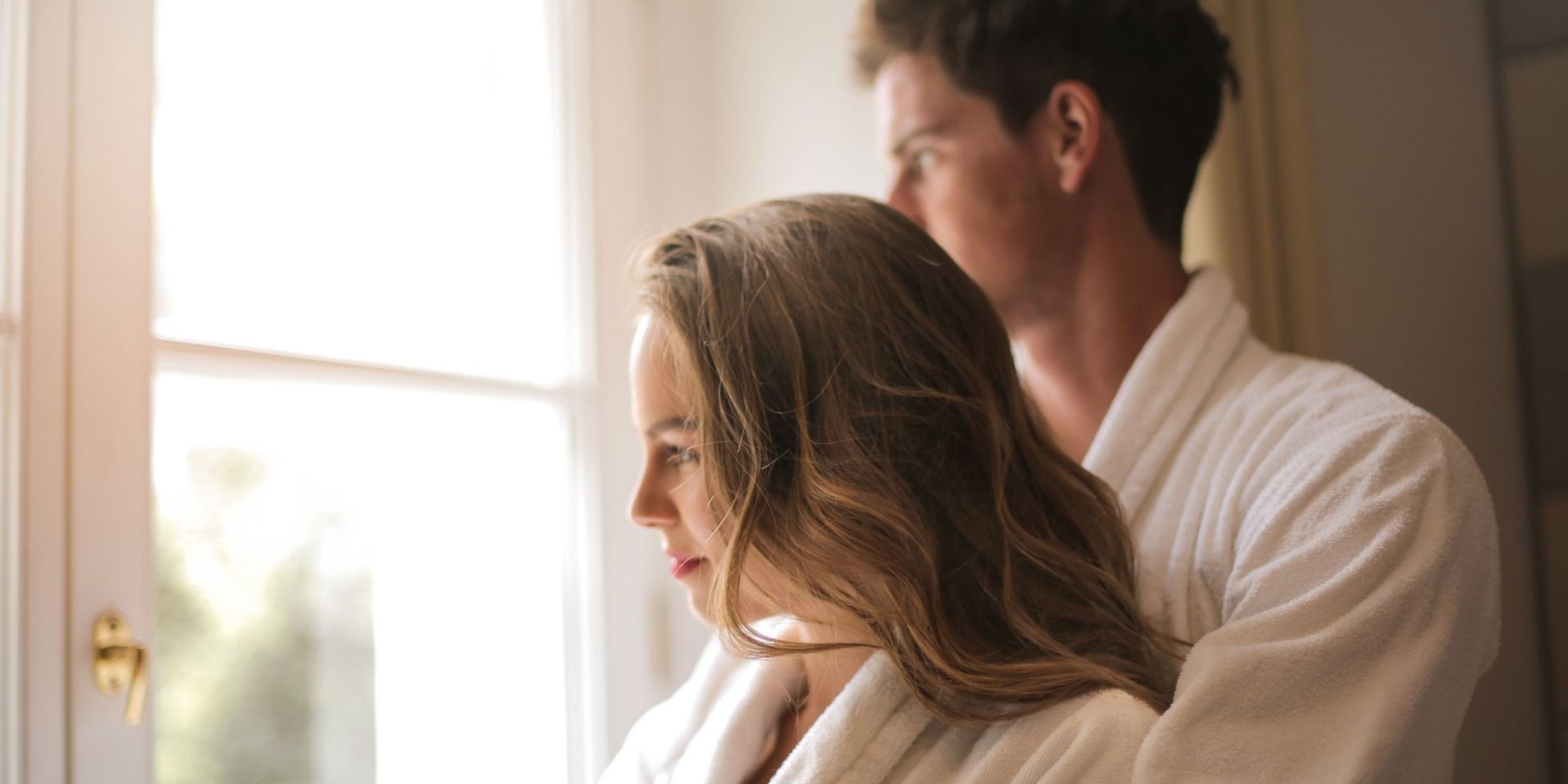 Una pareja con batas blancas, de pie juntos junto a una ventana iluminada por el sol | Fuente: Pexels