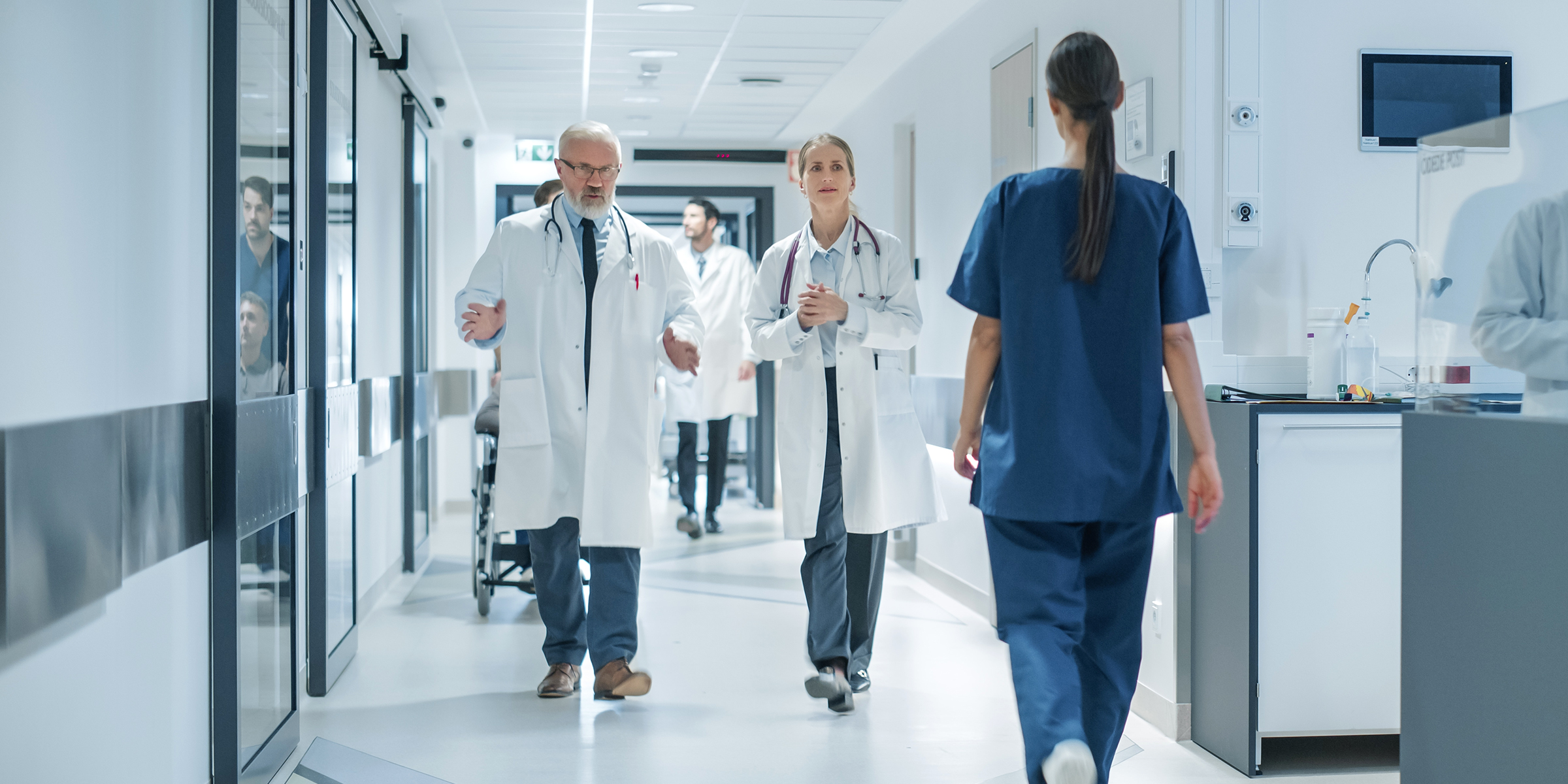 Personal sanitario por un pasillo de hospital muy iluminado durante un turno ajetreado | Fuente: Shutterstock