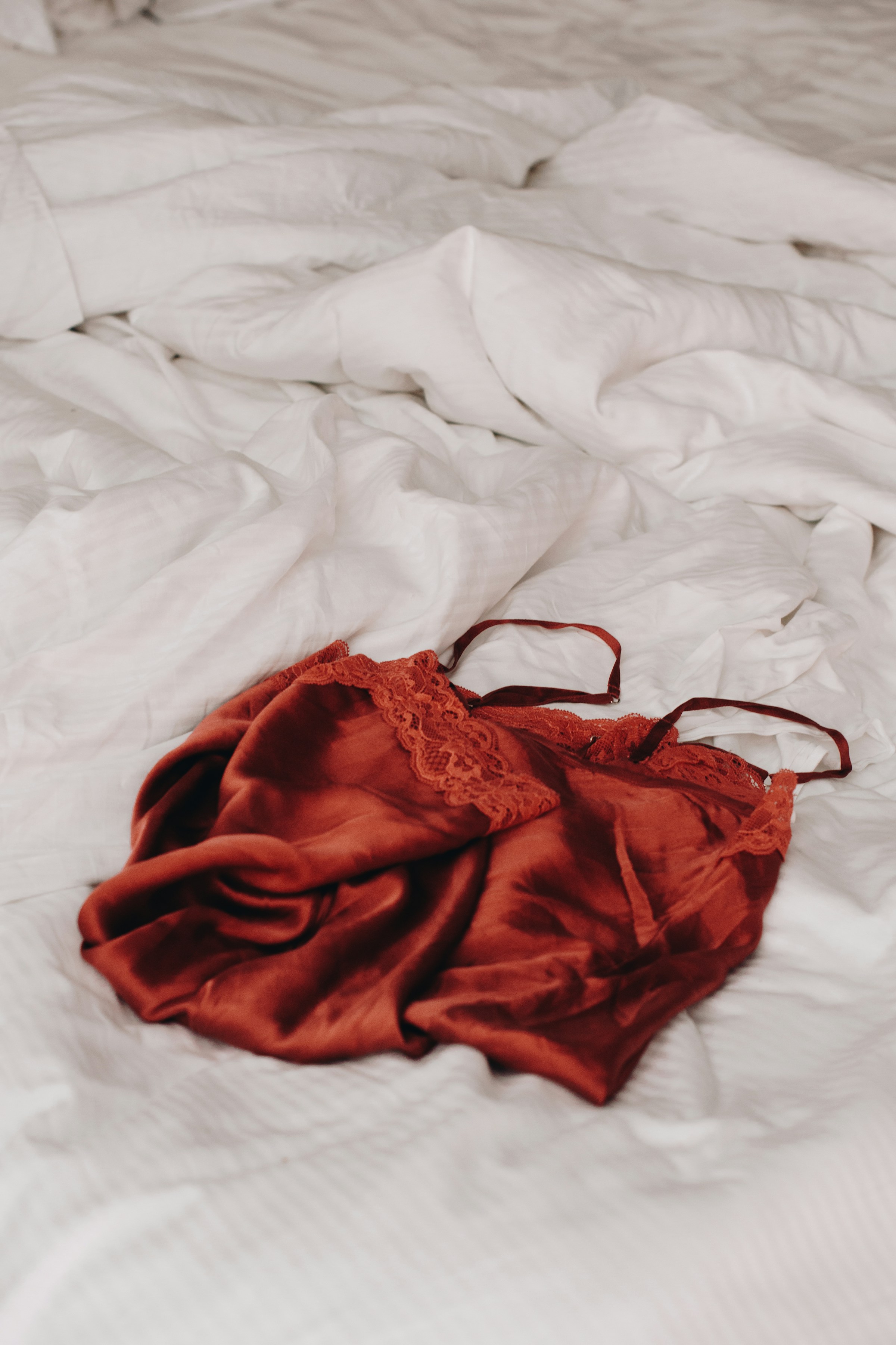 Lencería de encaje rojo tendida sobre sábanas de lino blanco | Foto: Unsplash