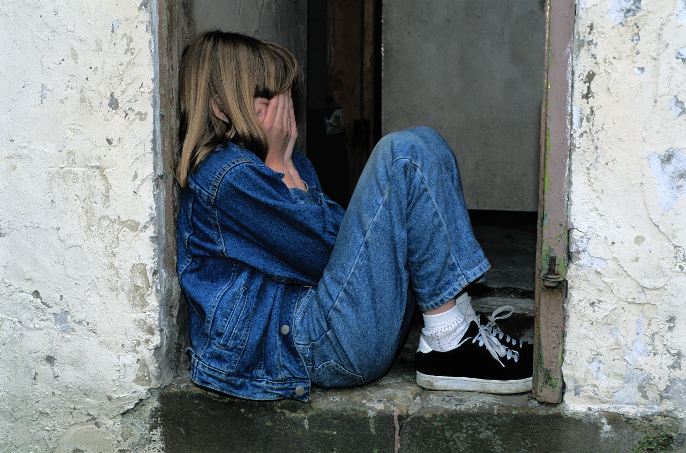 Niña triste sentada en medio de una puerta. | Foto: Pexels