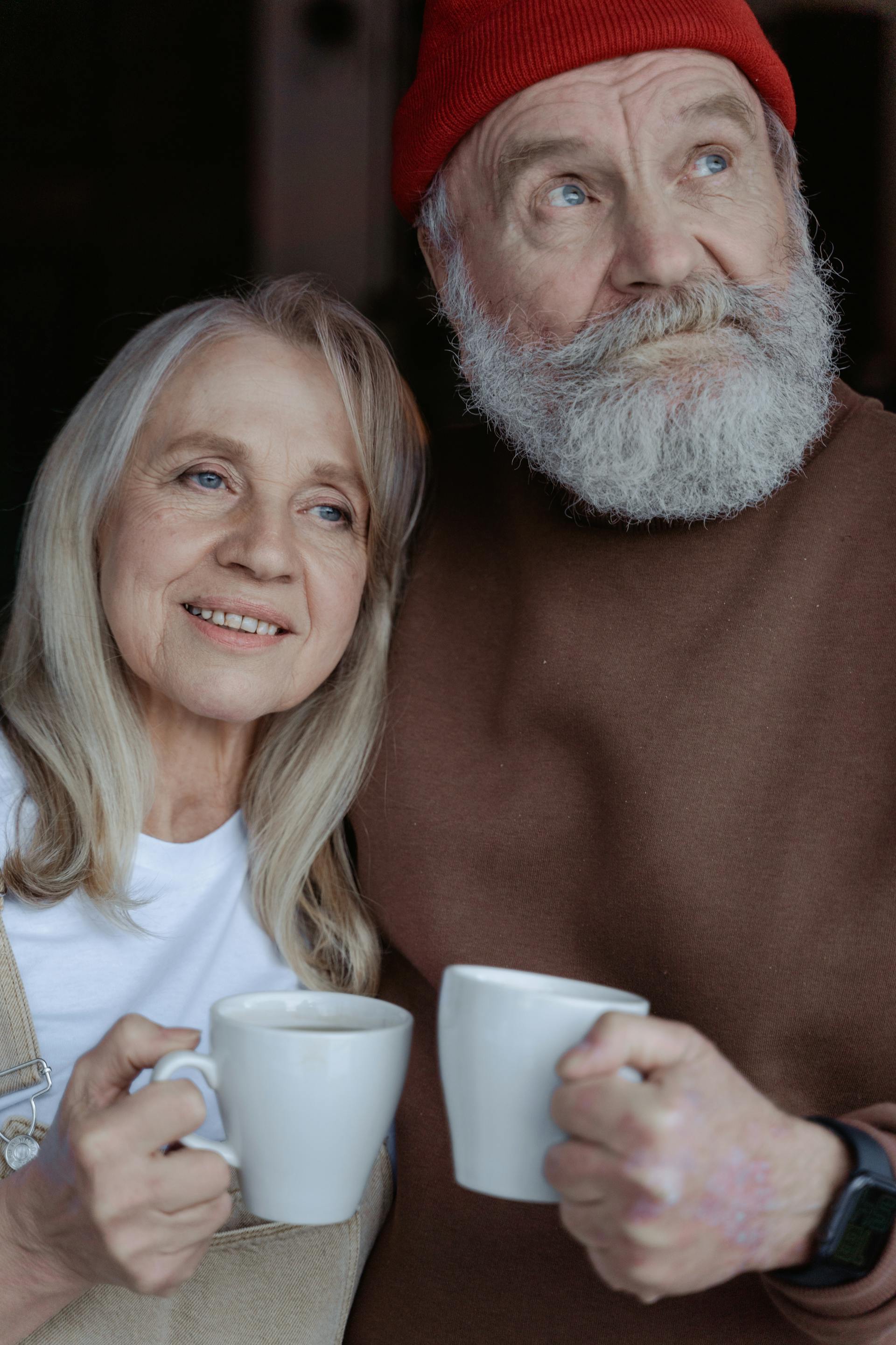 Pareja mayor sonriente sosteniendo tazas de cerámica | Fuente: Pexels