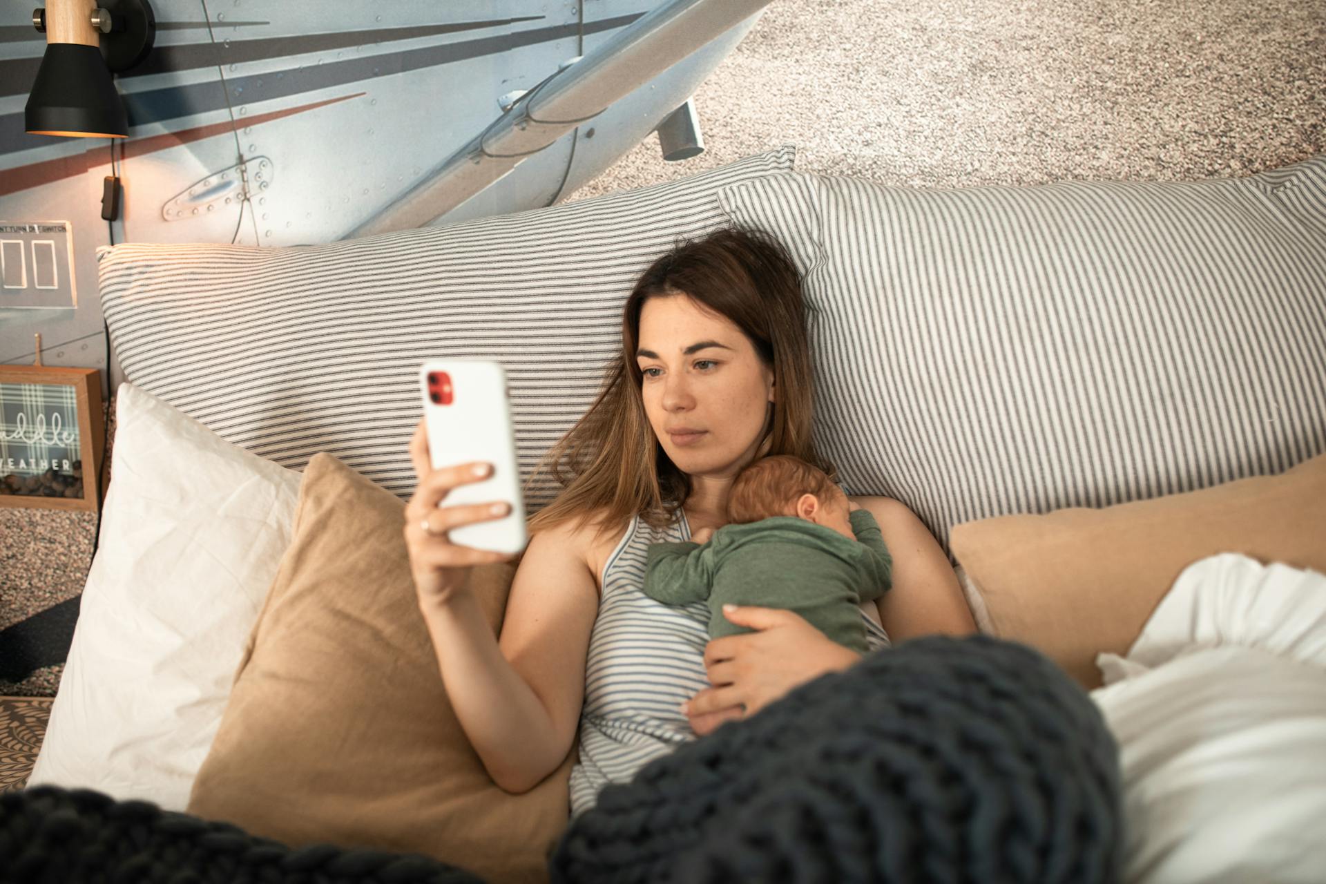 Una mujer tumbada y utilizando su teléfono con su bebé durmiendo sobre su pecho | Fuente: Pexels