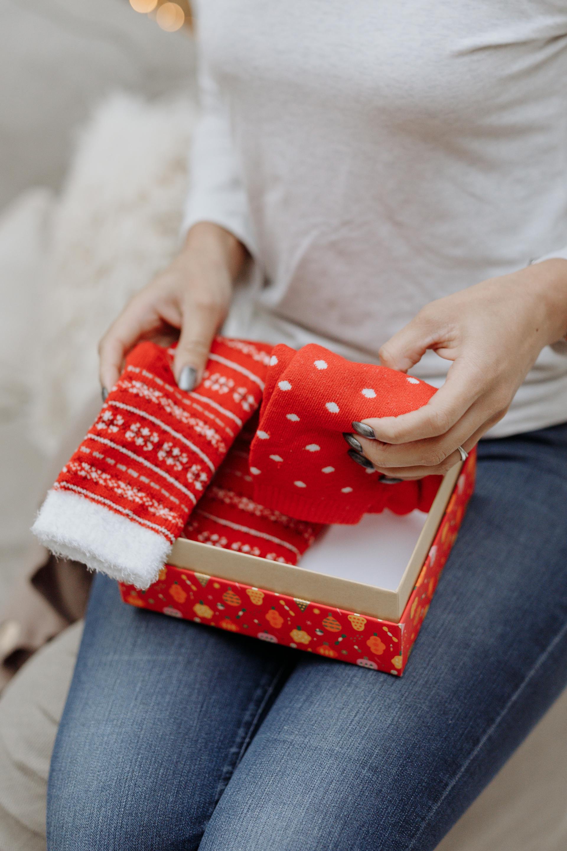 Primer plano de una mujer con calcetines de Navidad en una caja de regalo roja | Fuente: Pexels